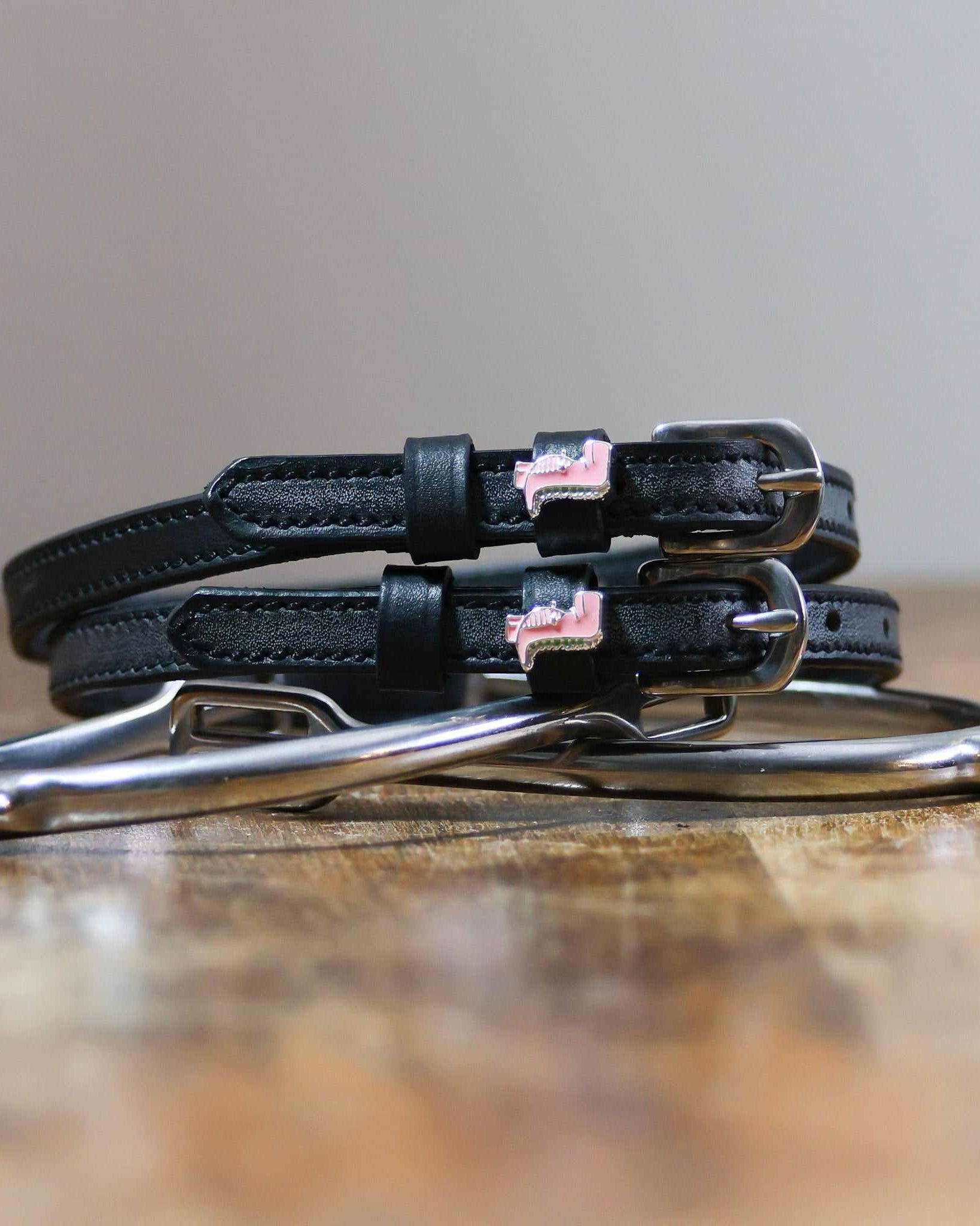 Pink dinosaur spur straps coiled on a silver stirrup on a wooden table