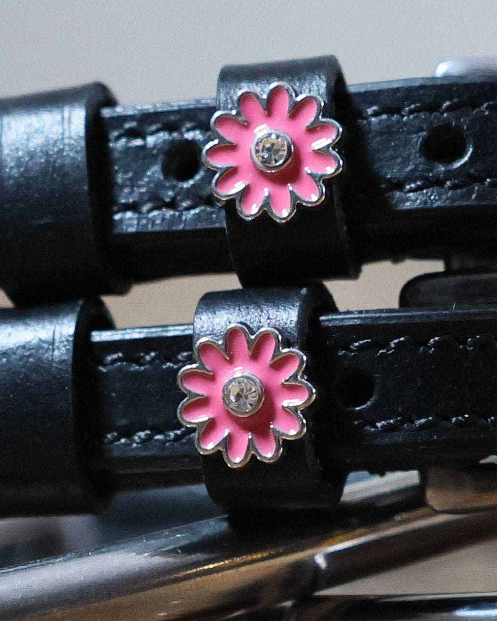 Close-up of pink daisy charms with rhinestone centers on black leather spur straps