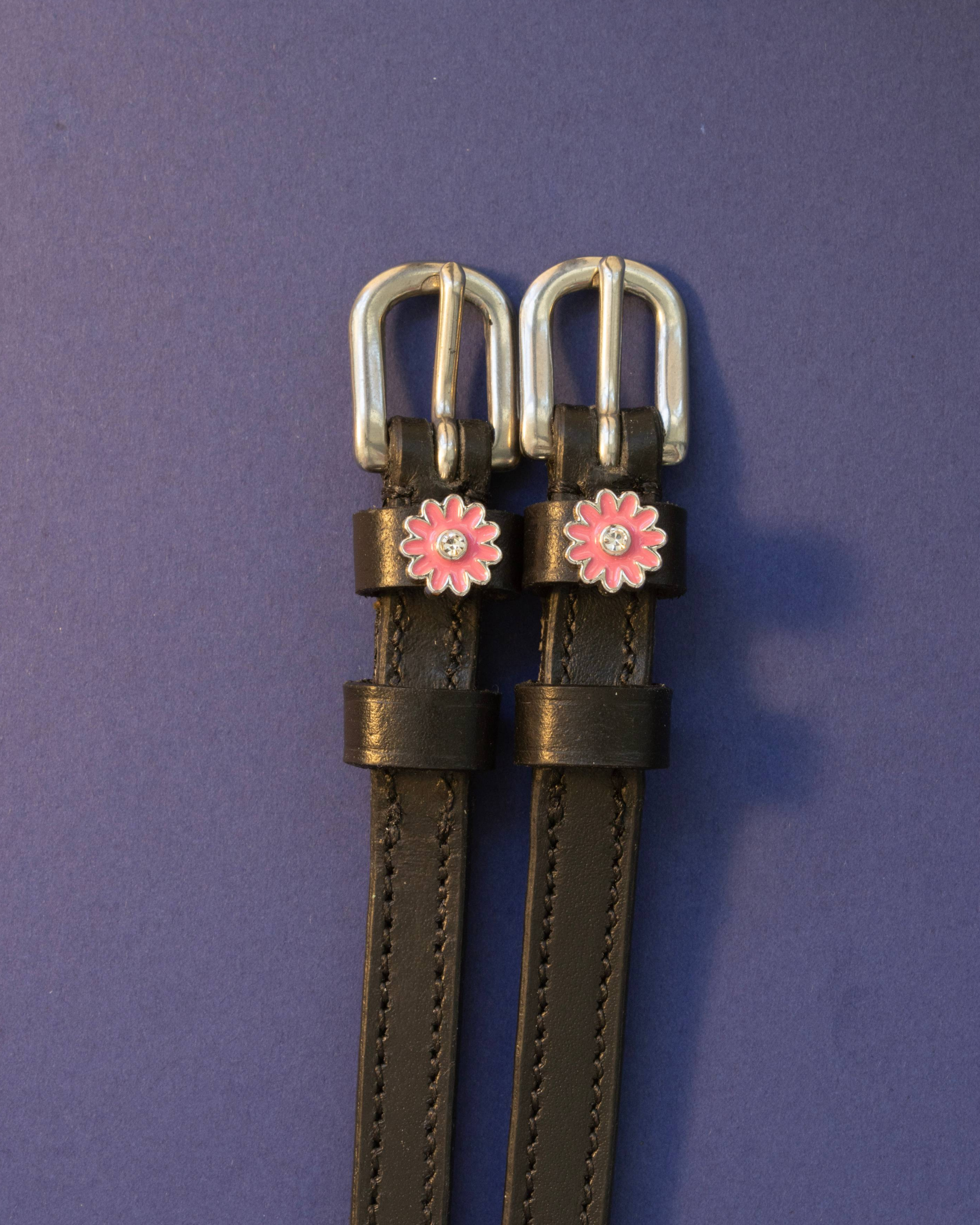 Black leather pink flower spur straps flat-laid on a deep purple background