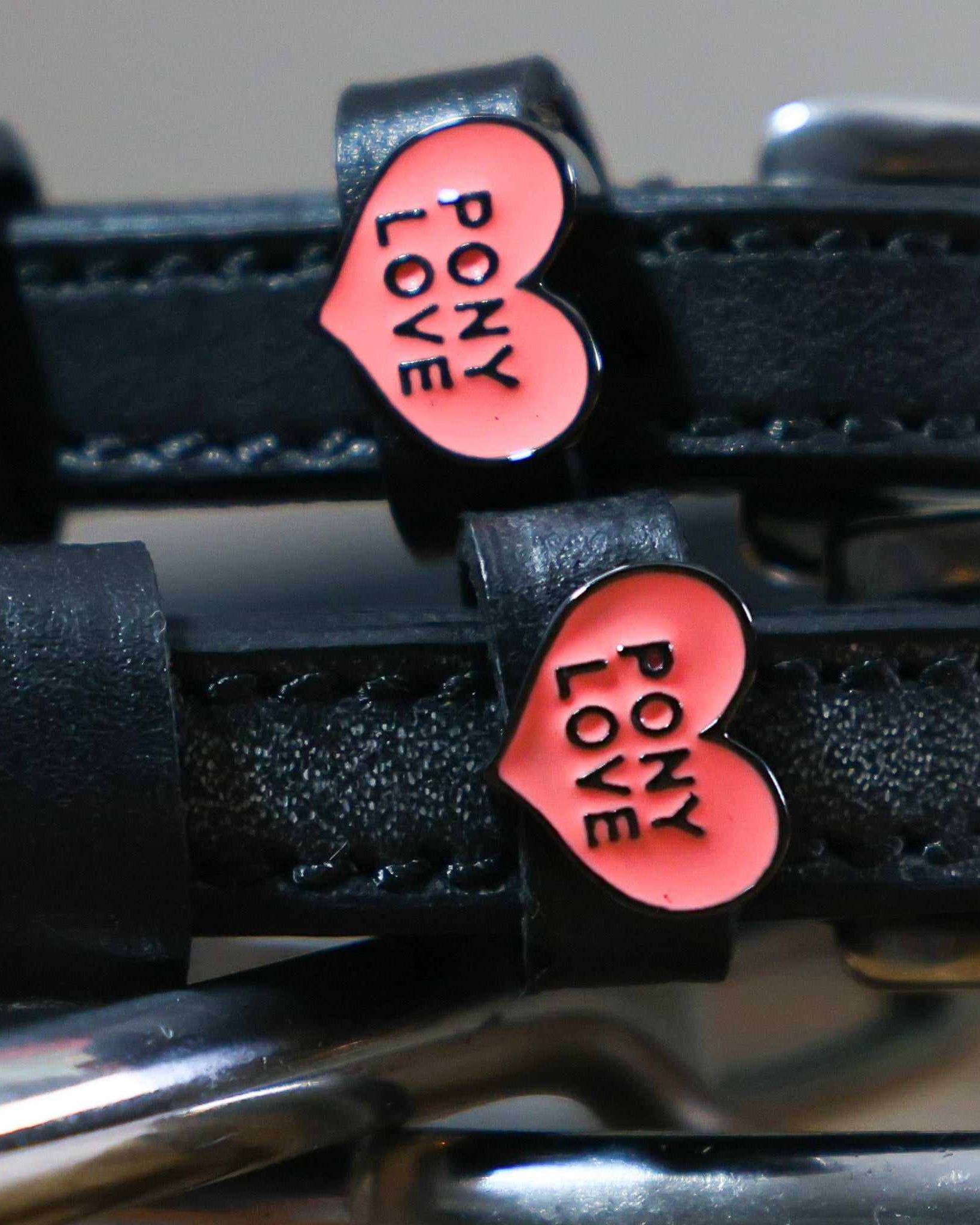 Close-up of pink Pony Love heart charms on black leather ManeJane spur strap keepers