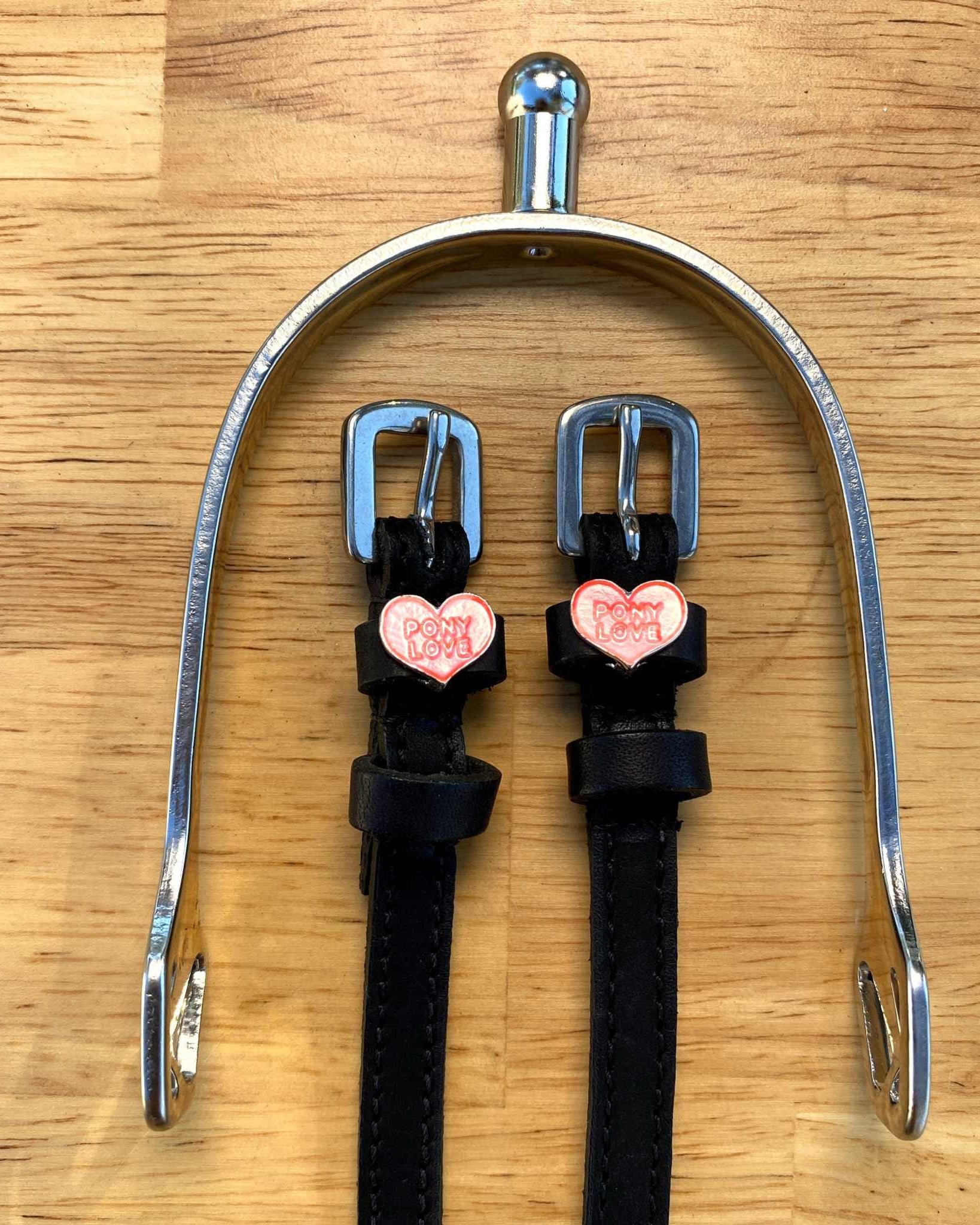 Pony Love spur straps hung from a silver spur bracket on a wood surface