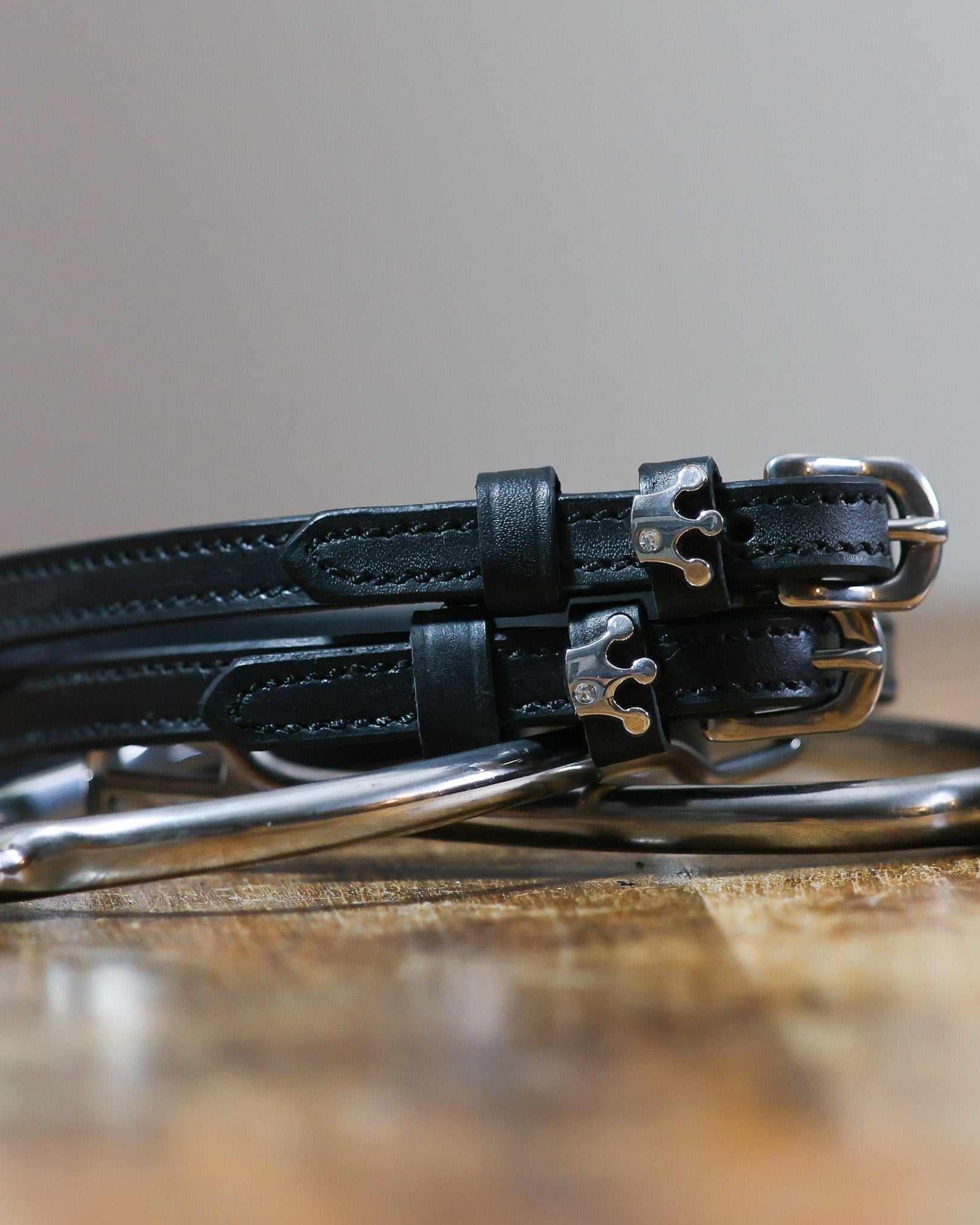Queenie crown-charm spur straps coiled beside a stirrup on a wooden tabletop