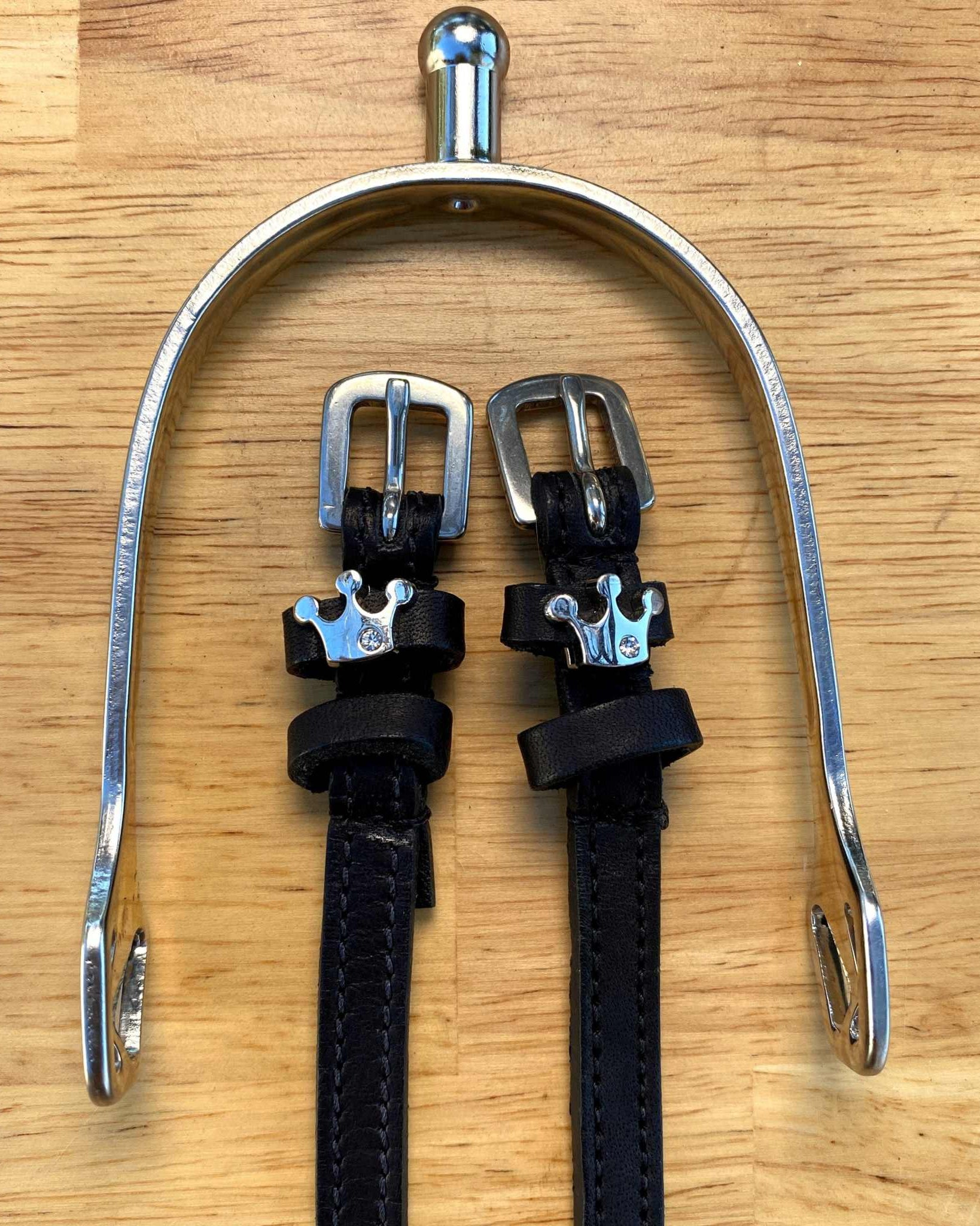 Queenie crown spur straps hung from a silver bracket on a wooden tabletop