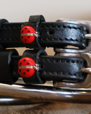 Close-up of red ladybug charms on black leather spur strap keepers