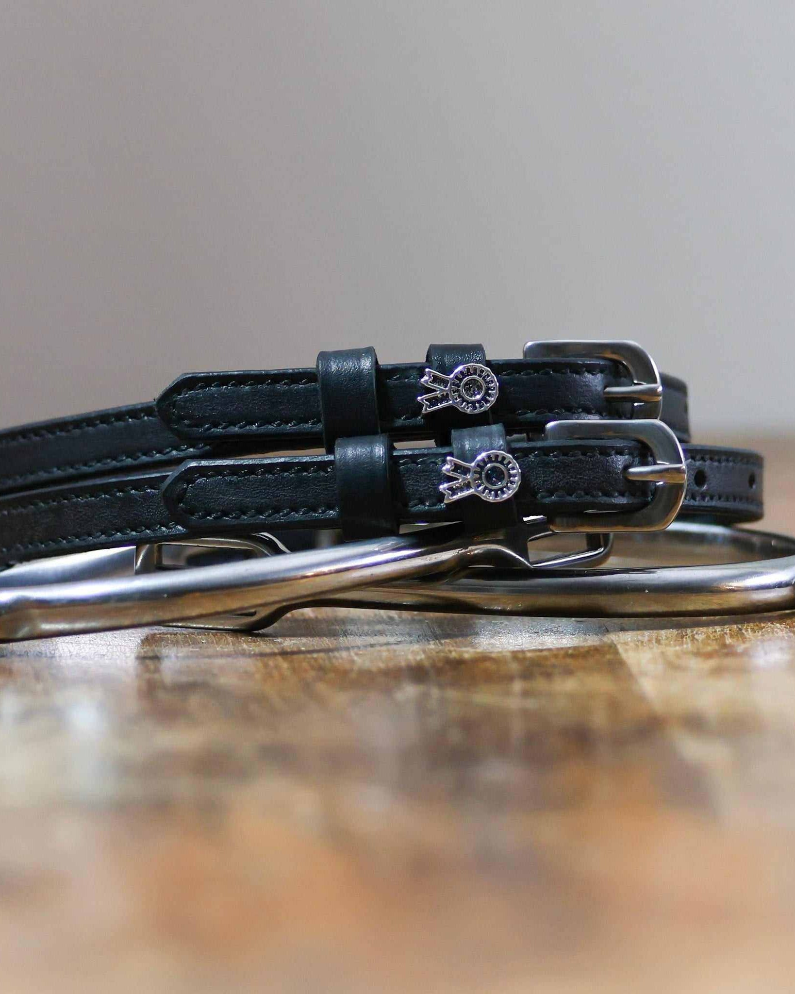 Black rosette charm spur straps coiled beside a silver spur on a wood surface