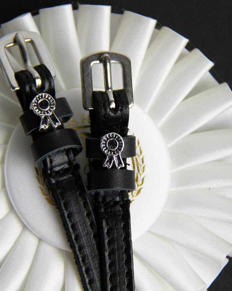 ManeJane rosette spur straps arranged over a white prize ribbon, black background