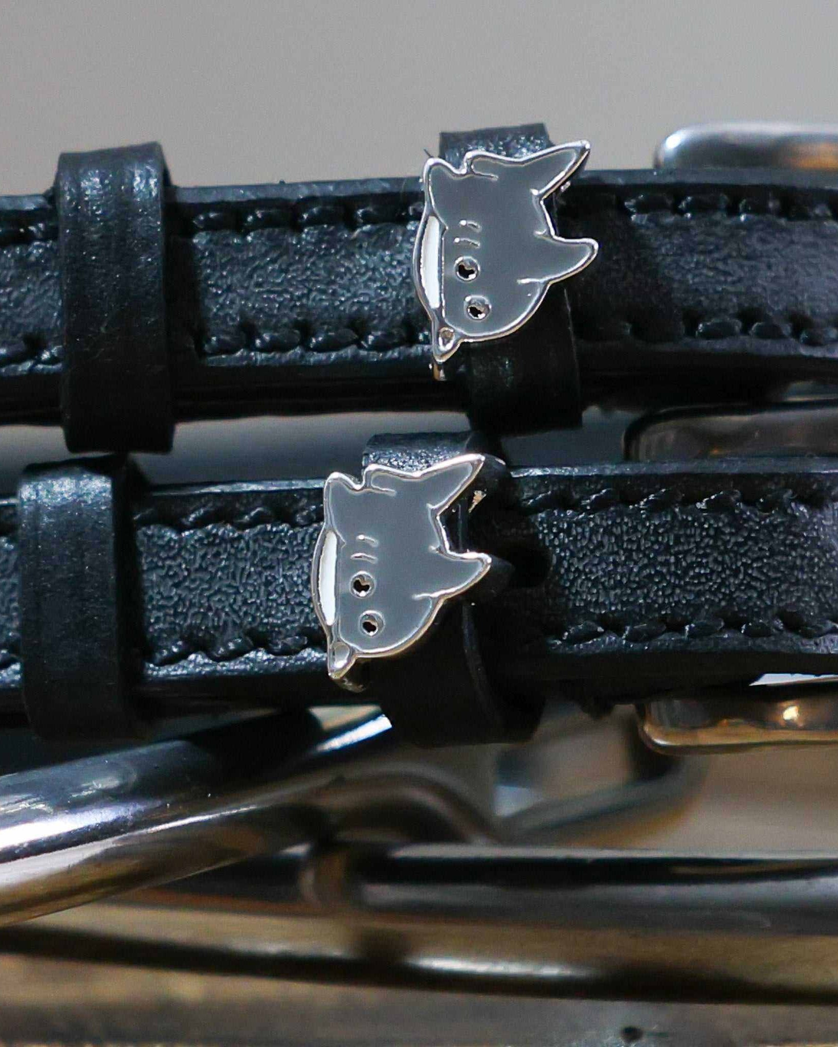Close-up of silver shark charms on black leather spur strap keepers with hardware
