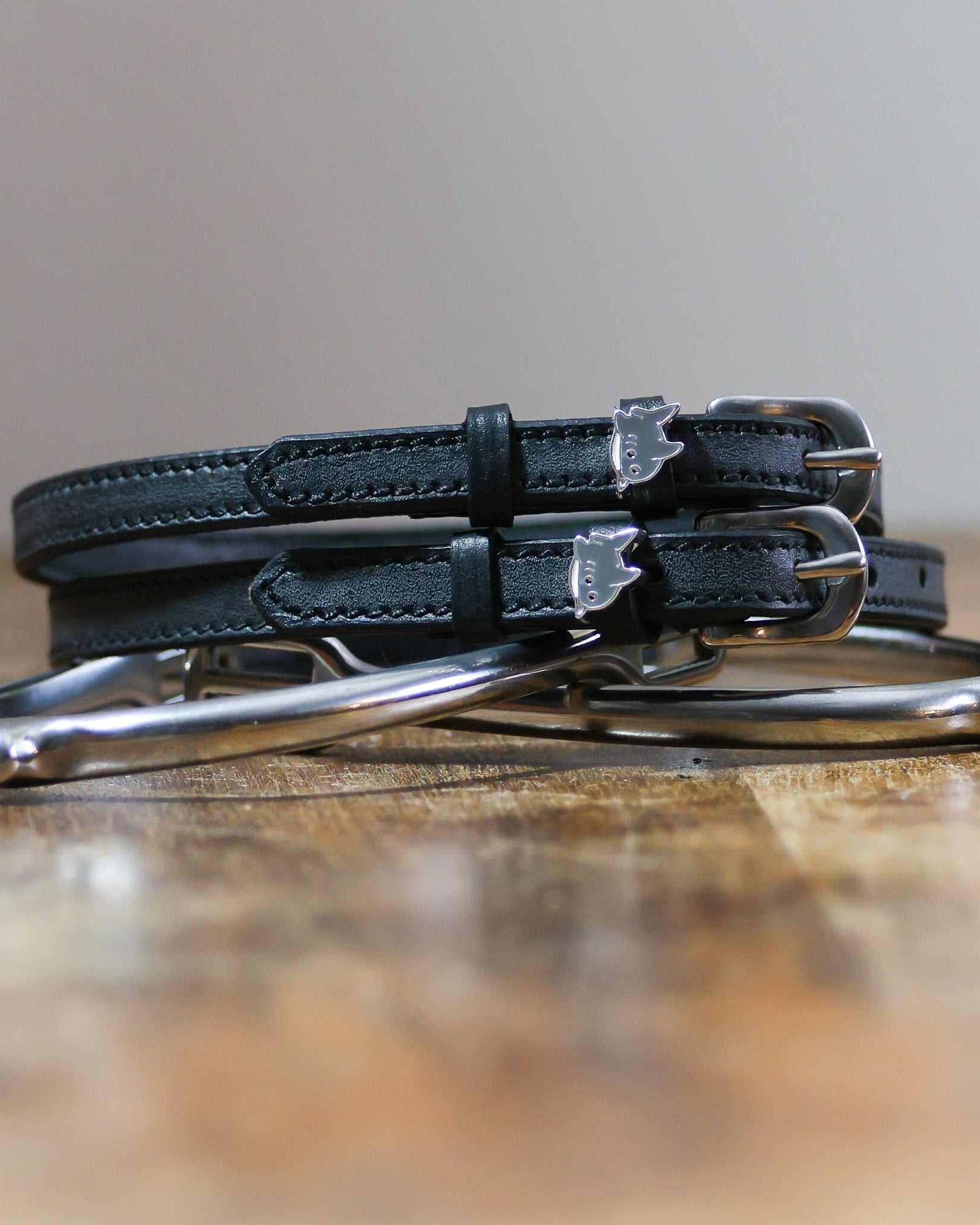 Black shark charm spur straps coiled beside a silver spur on a rustic wood surface