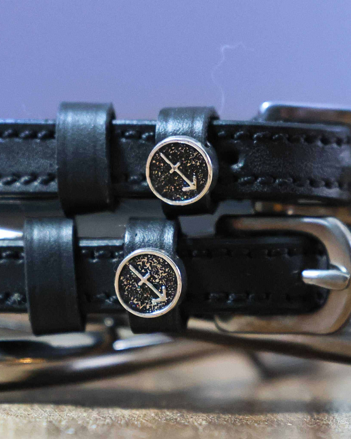 Close-up of Sagittarius arrow zodiac charms on black leather spur strap keepers