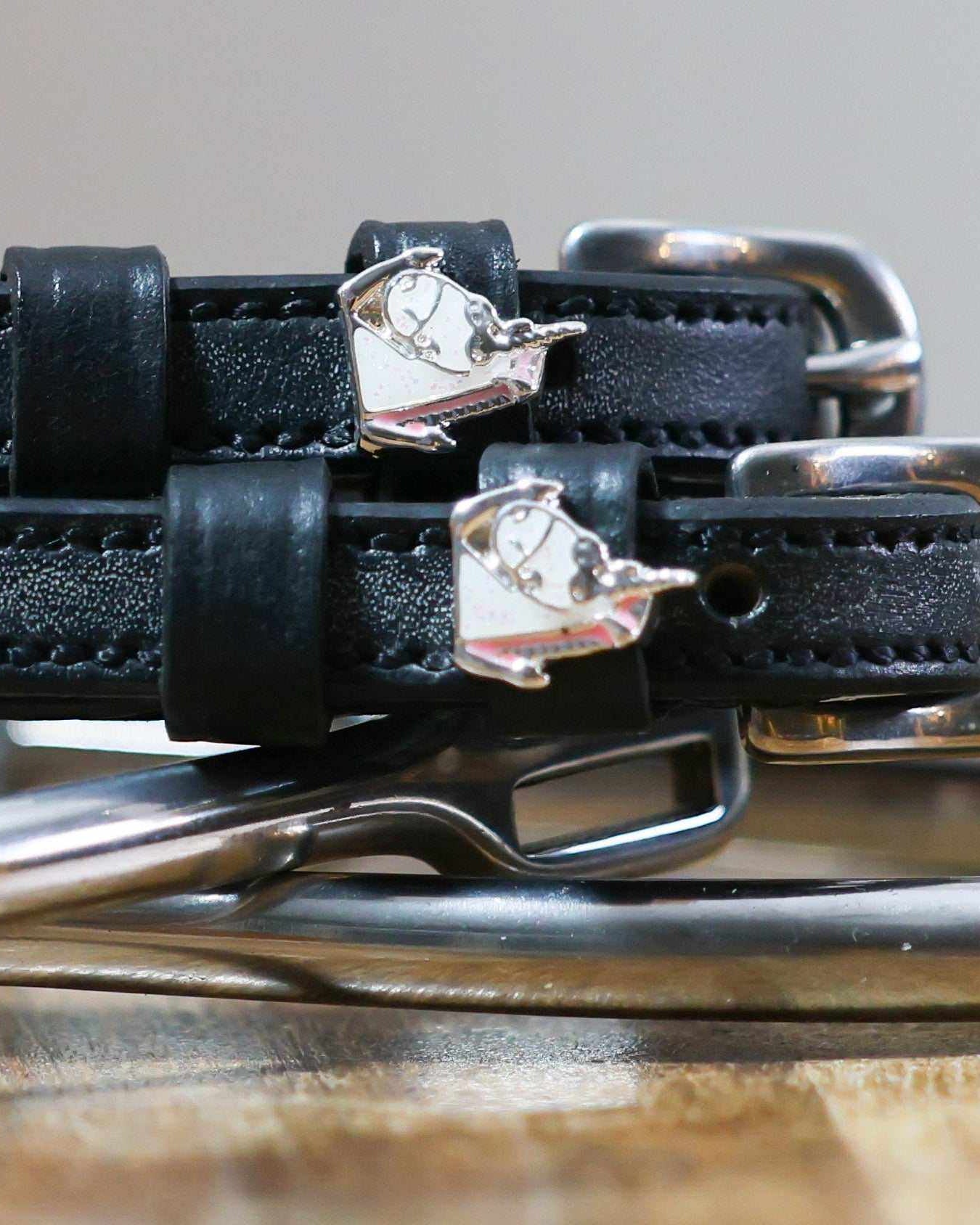 Close-up of silver enamel unicorn charms on black leather ManeJane spur strap keepers