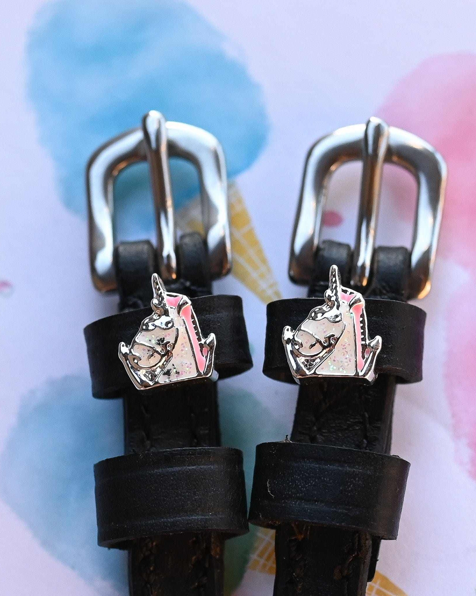 Silver unicorn head charms on black leather spur straps over a pastel watercolor background
