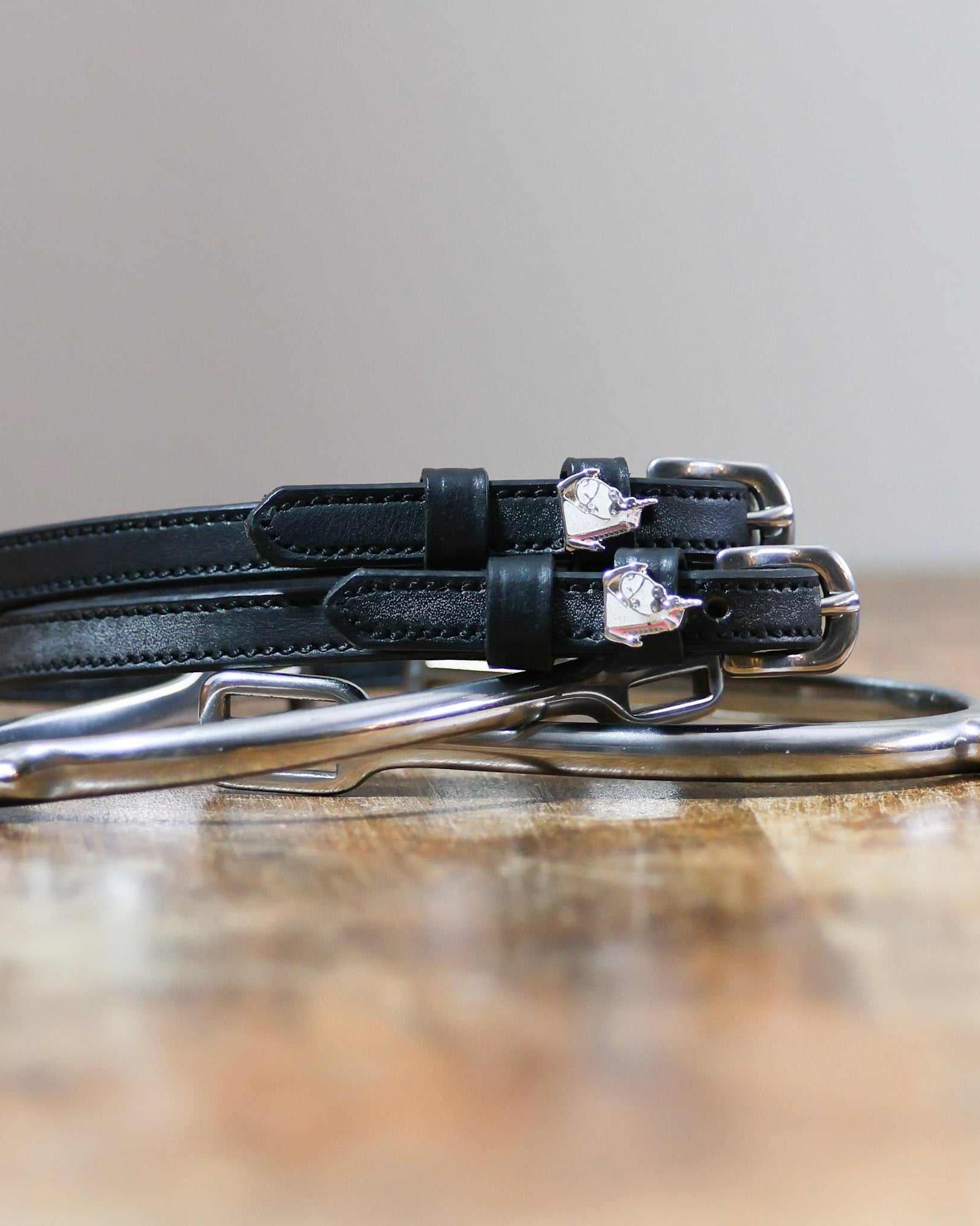 Black unicorn charm spur straps coiled beside silver spurs on a rustic wood surface