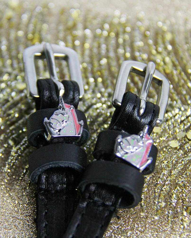 Close-up of silver unicorn charms on black leather spur straps against gold glitter