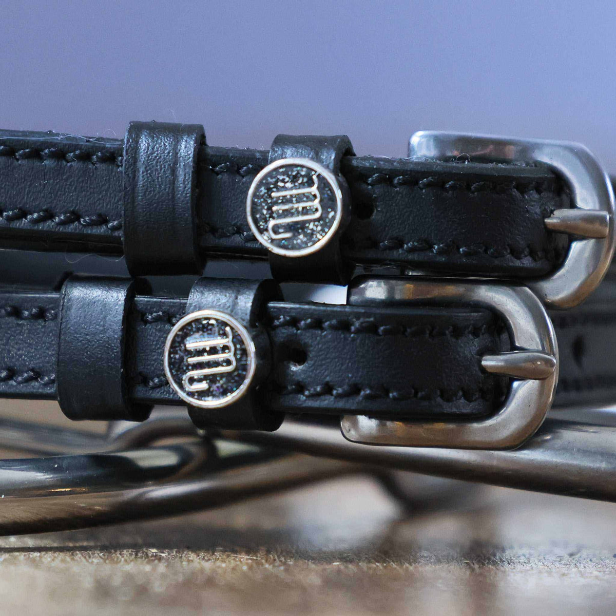 Close-up of silver Scorpio zodiac medallion charms on black leather ManeJane spur straps