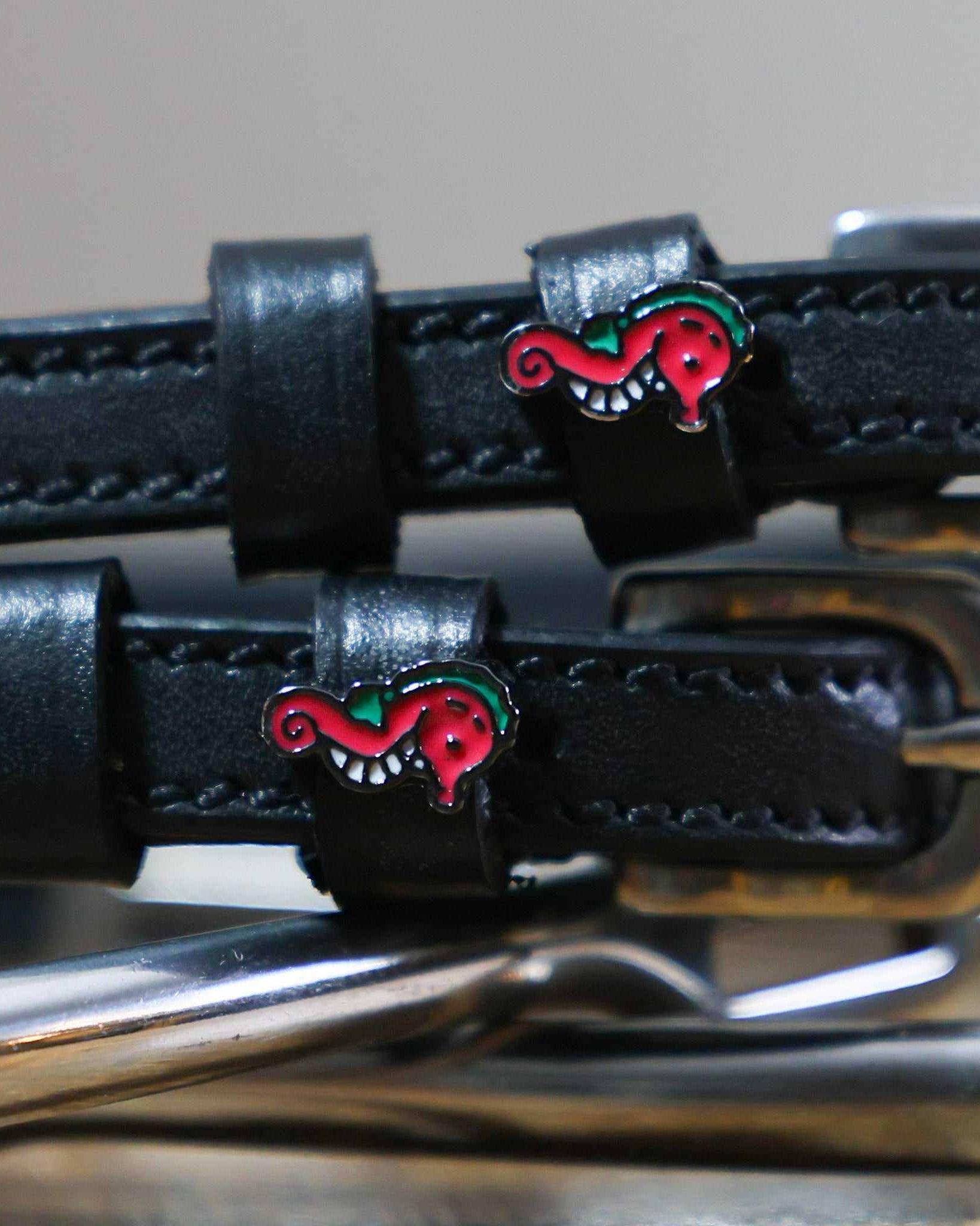 Close-up of pink seahorse charms on black leather spur strap keepers beside a stirrup