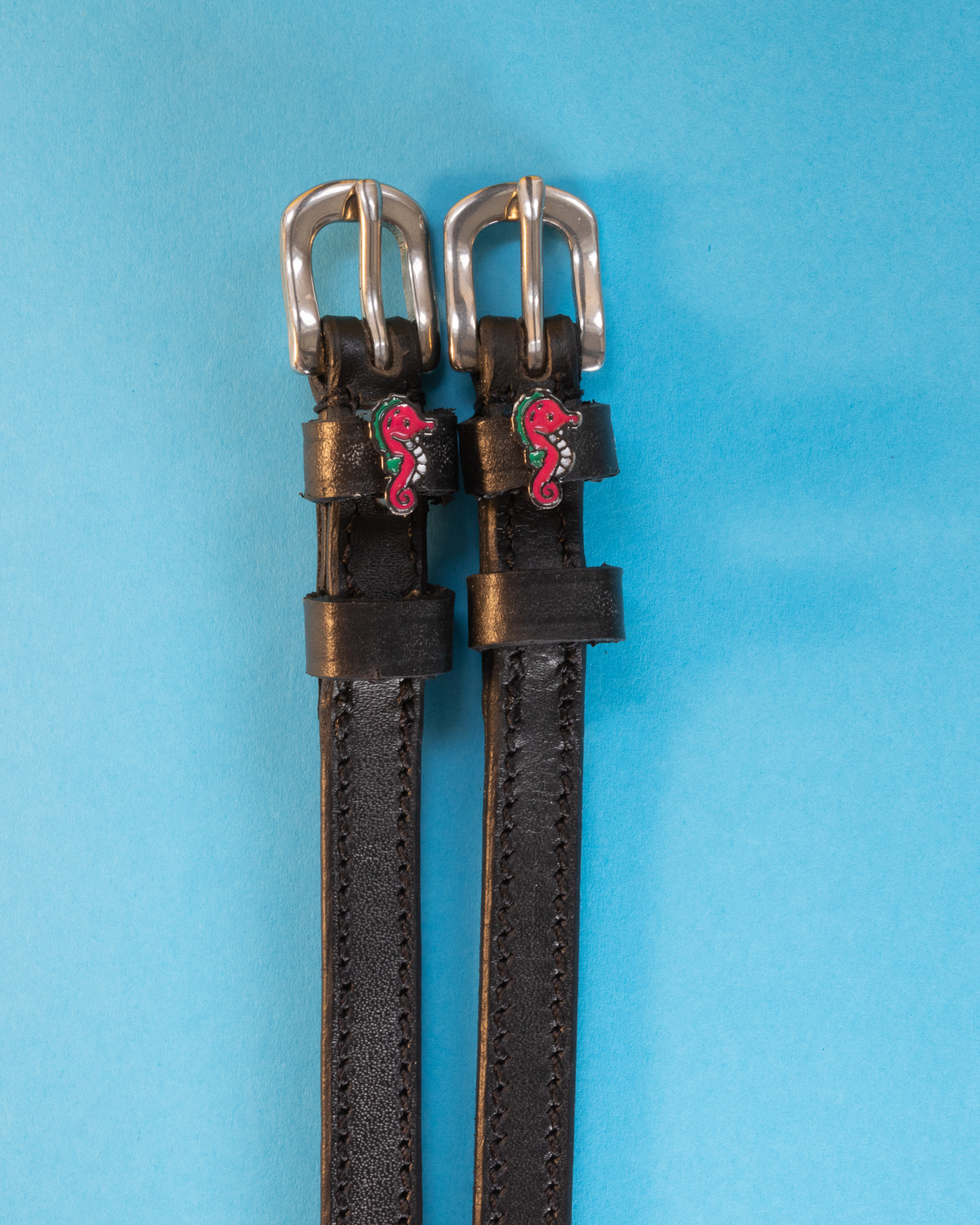 Black leather ManeJane seahorse spur straps on a bright blue background