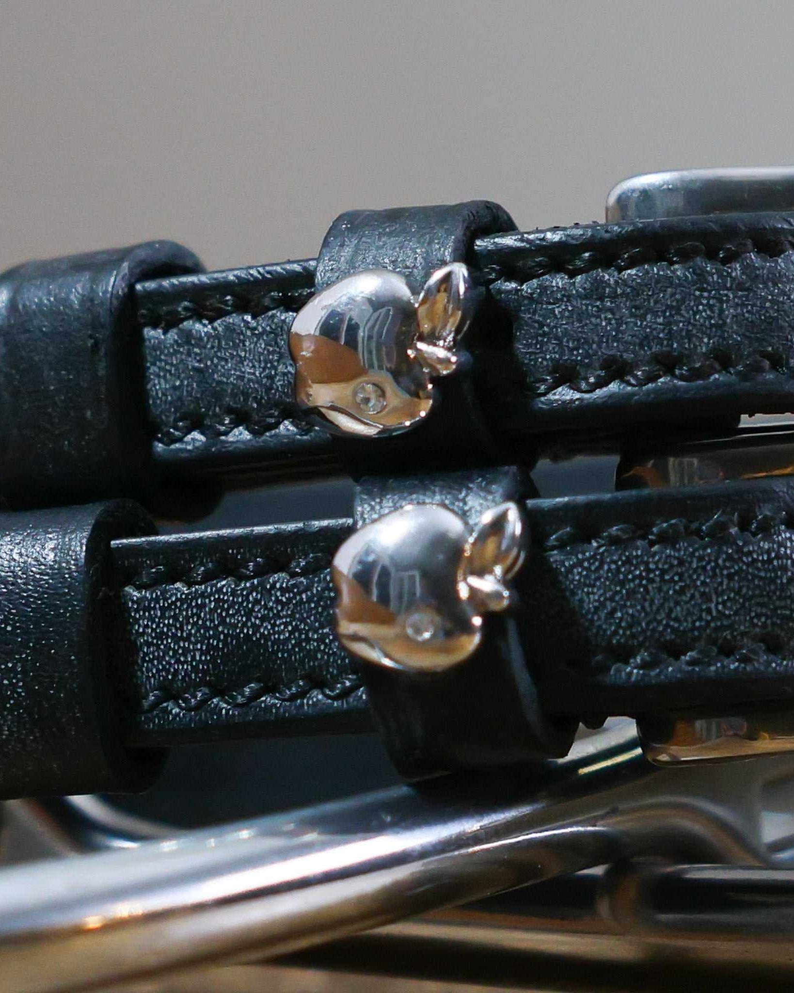 Close-up of shiny silver apple charms on black leather spur strap keepers