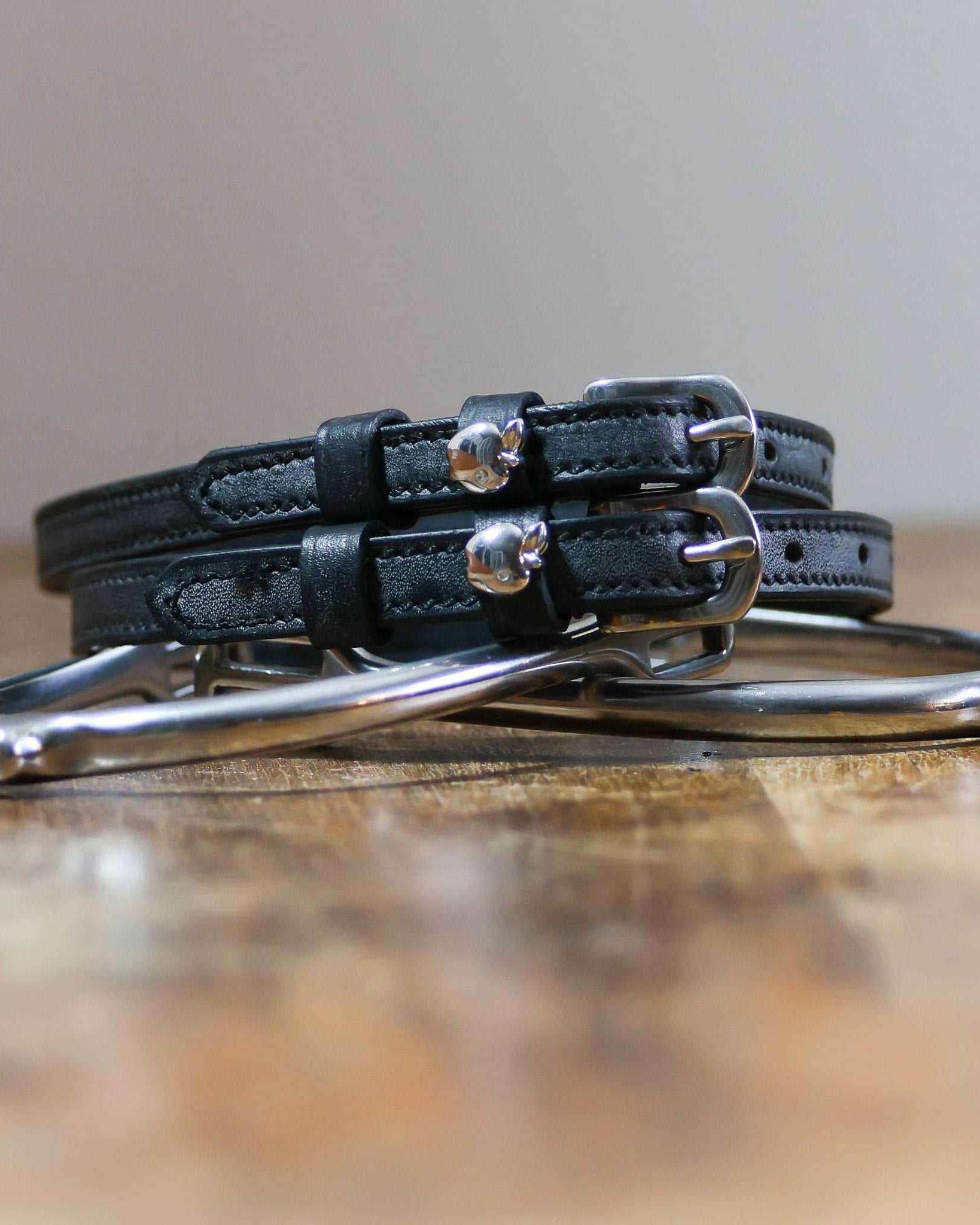 Silver apple spur straps coiled on a stirrup on a wooden table