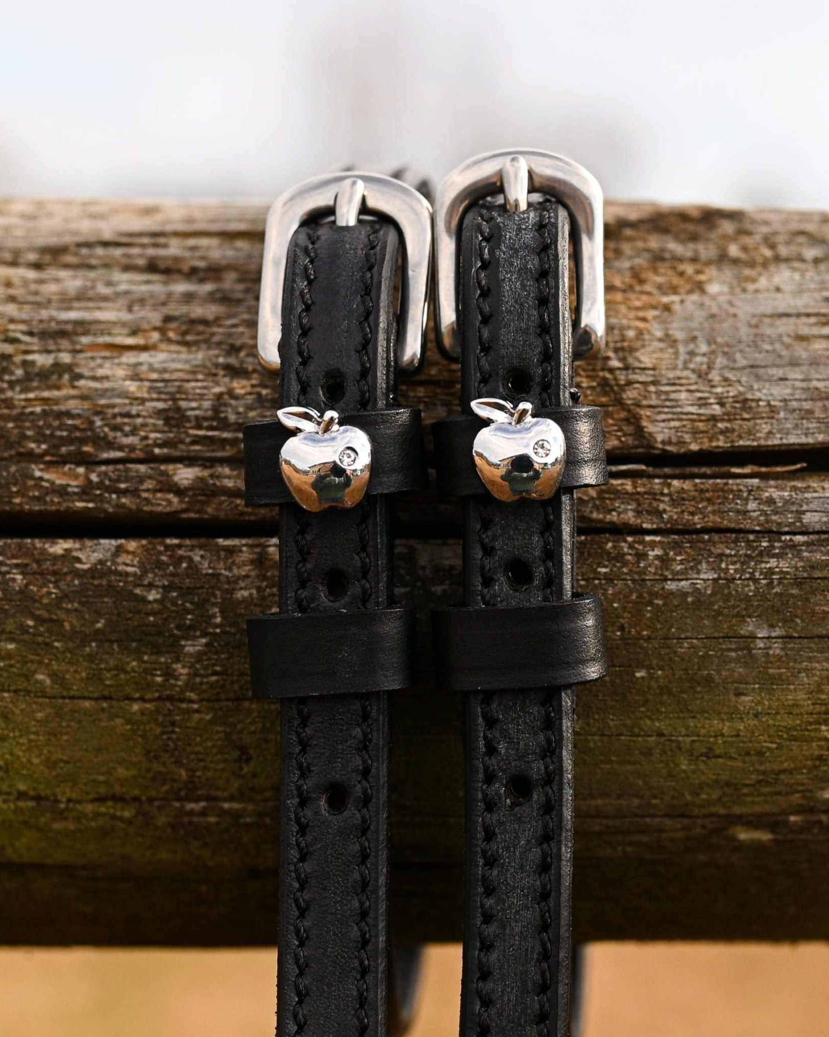 Black leather silver-apple spur straps with buckles draped over a weathered wood rail
