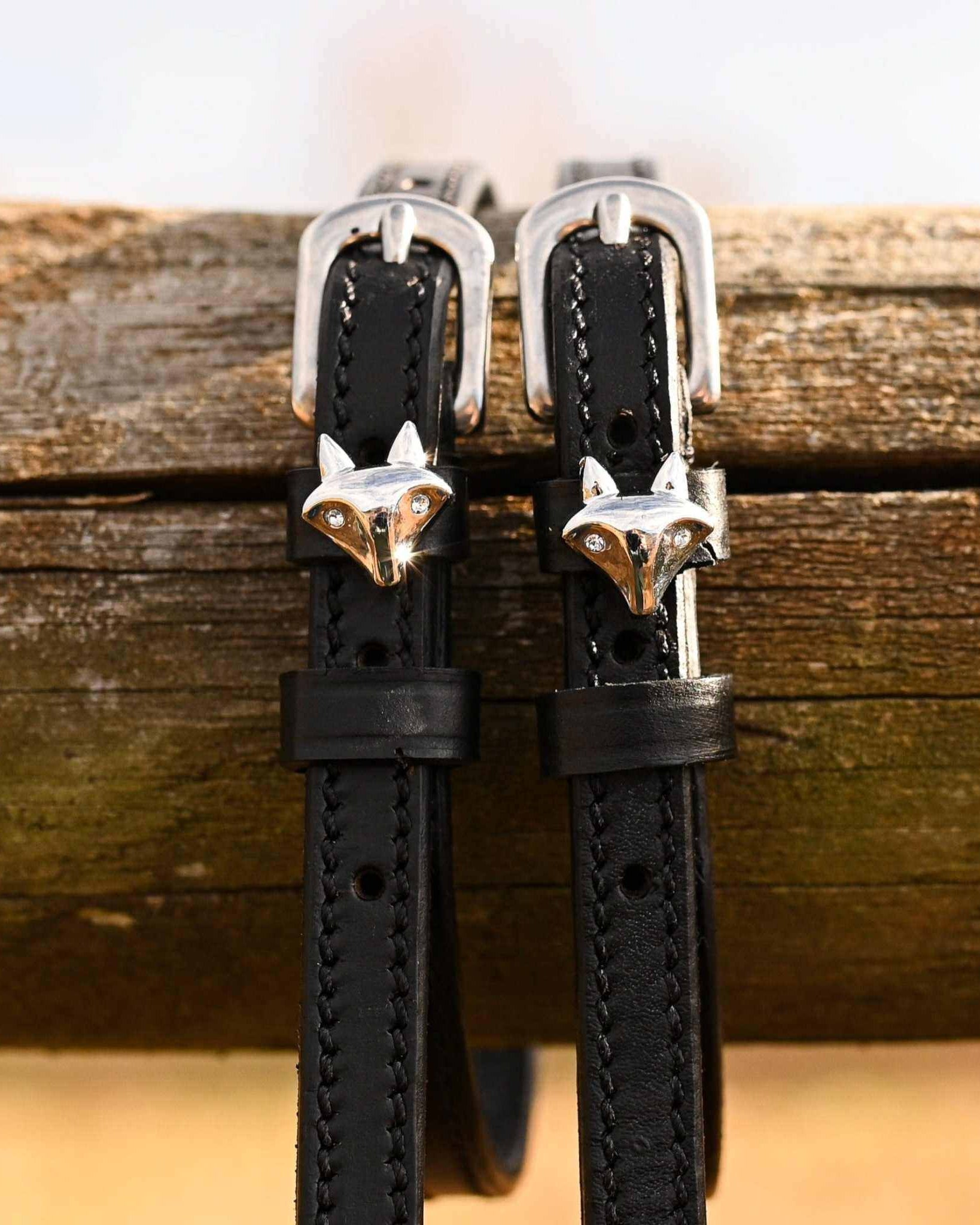 Black leather silver fox spur straps hanging over a weathered wooden fence rail