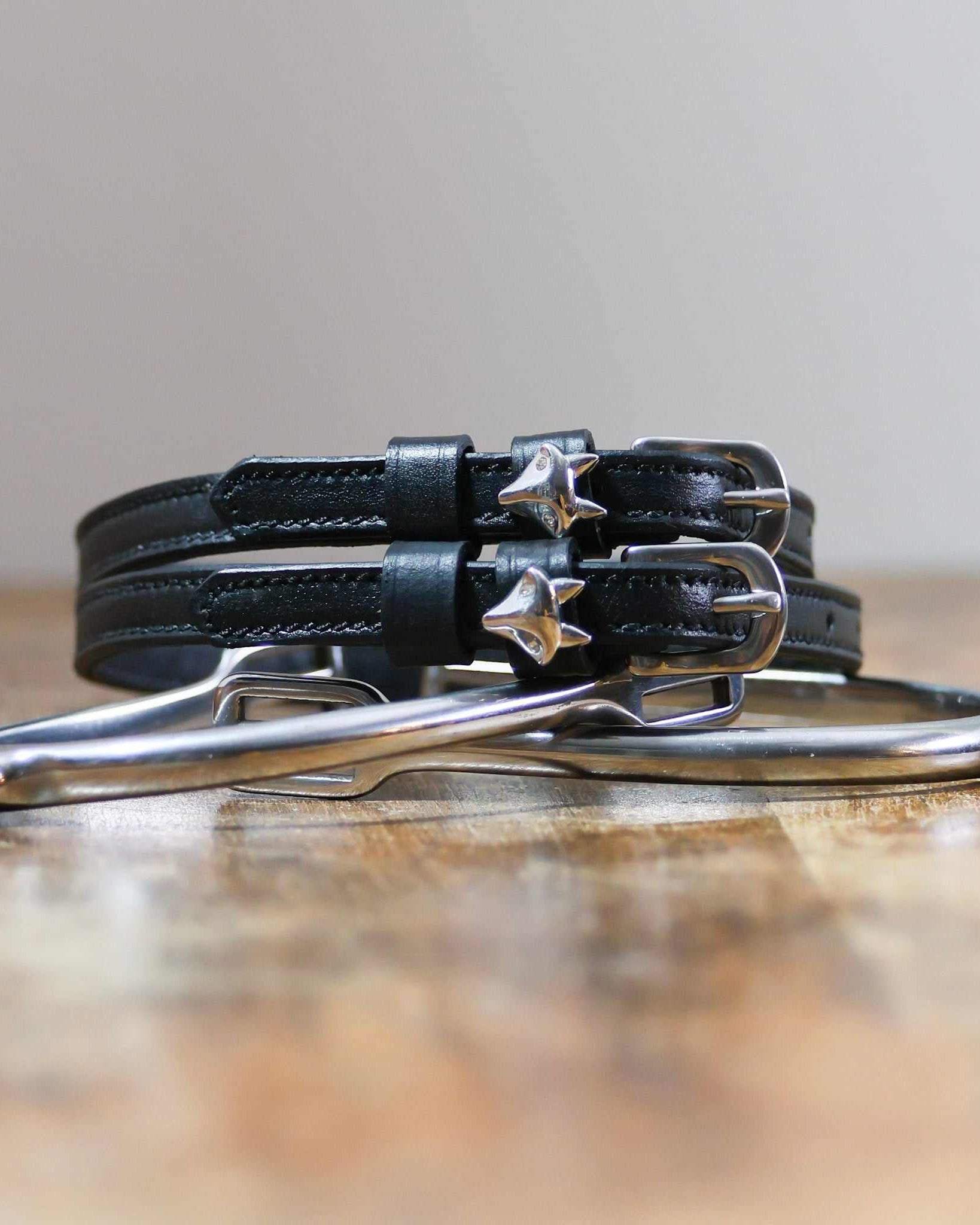 Coiled black leather ManeJane silver fox spur straps stacked on a spur on a wooden table
