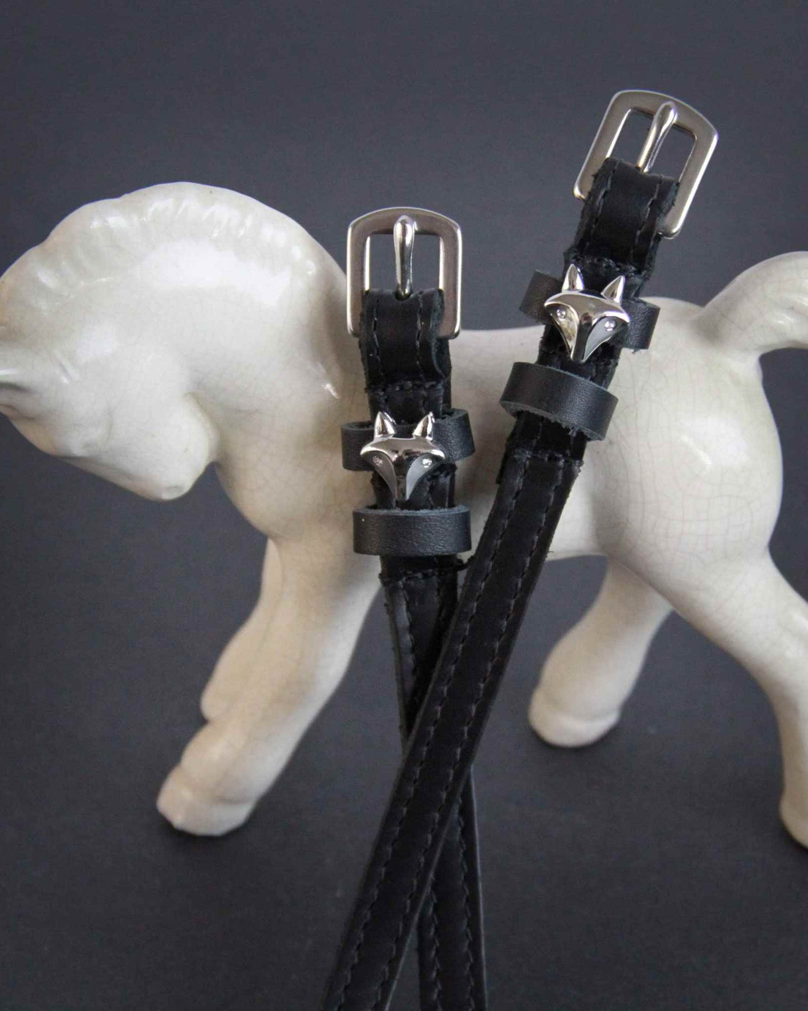 Black leather silver fox spur straps draped over a white ceramic foal figurine