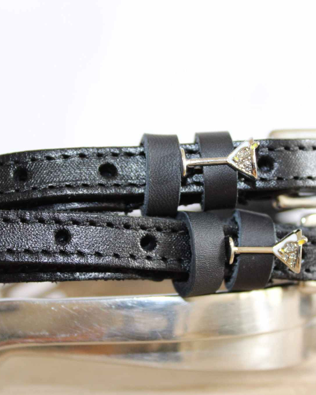 Black martini glass spur straps resting on a polished silver spur, close-up