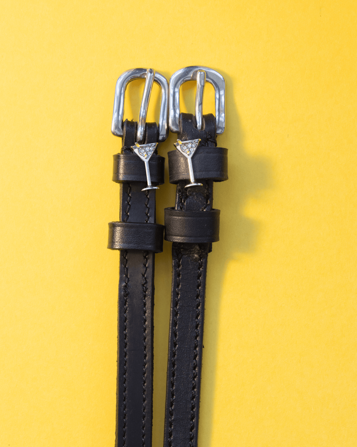Pair of black leather martini glass spur straps laid flat on a yellow background