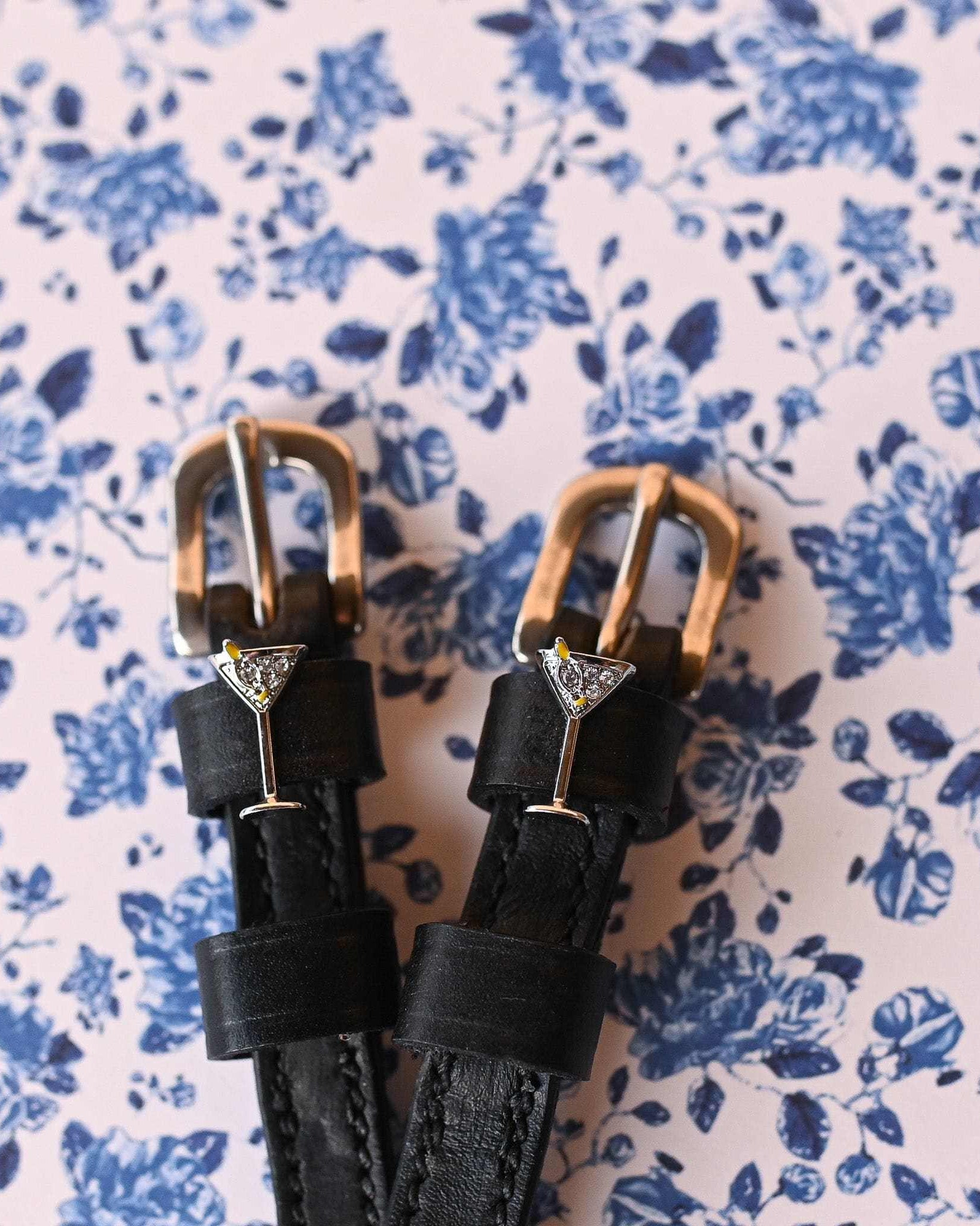 Martini glass ManeJane spur straps with brass buckles on blue floral wallpaper