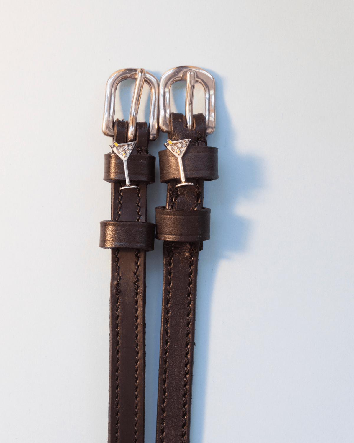 Dark brown leather martini glass spur straps with silver buckles on off-white