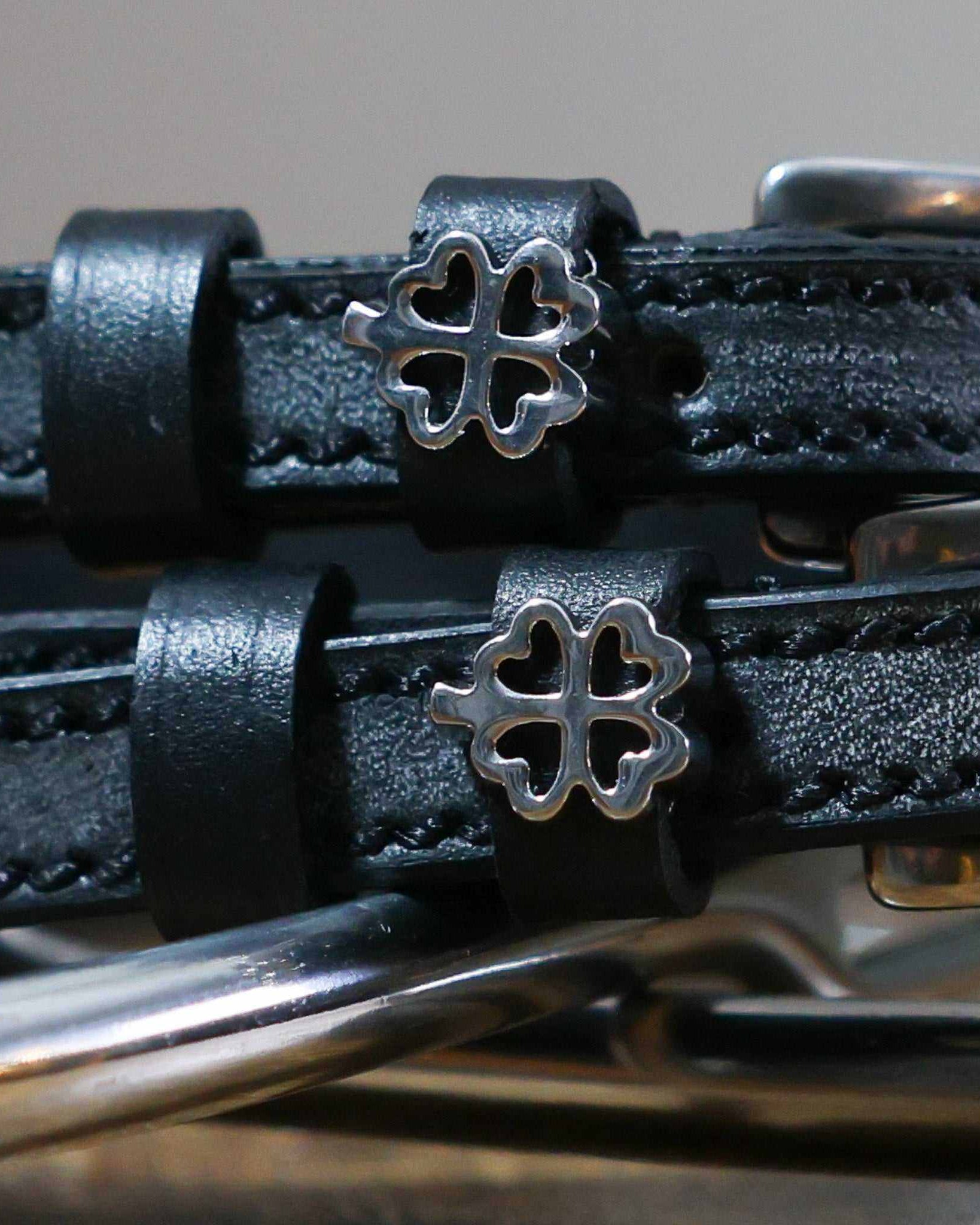 Close-up of silver outline clover charms on black leather ManeJane spur straps