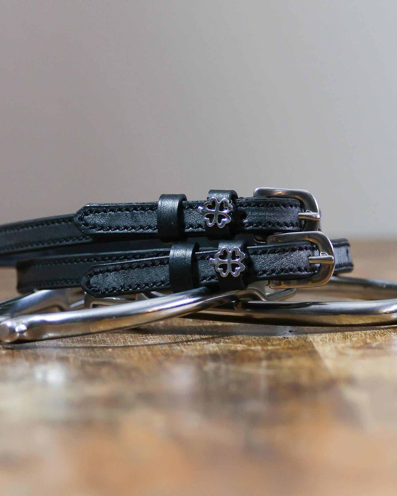 Coiled black leather clover spur straps on a silver spur, openwork silver clover charms