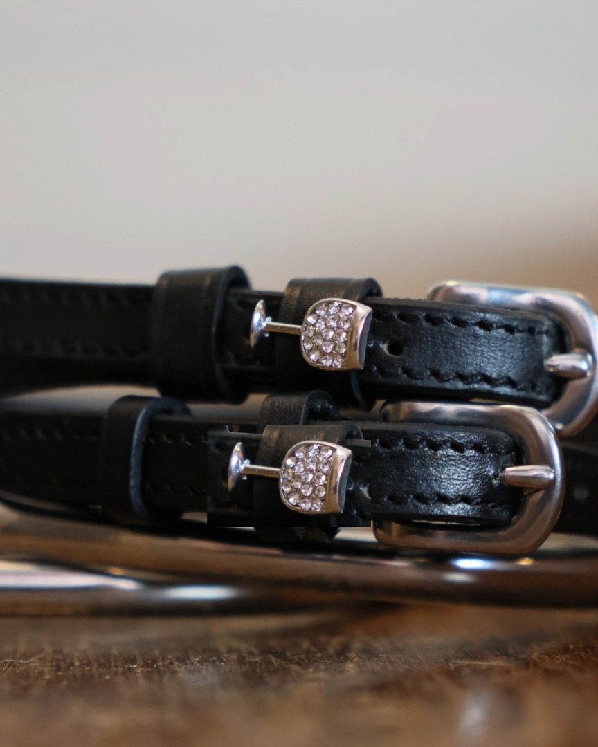 Black leather wine glass spur straps coiled beside a silver spur on a wooden surface