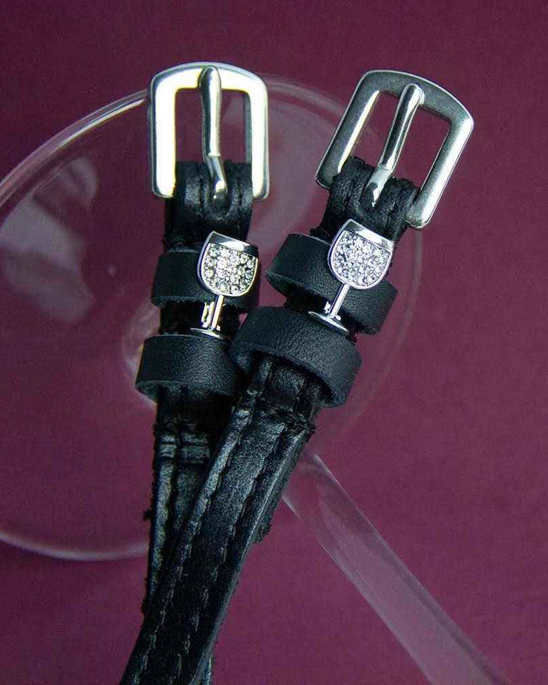 Close-up of crystal wine glass charms on black leather spur straps on burgundy