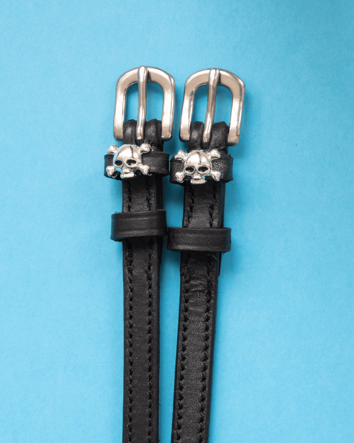 Pair of black leather skull and crossbones spur straps with silver buckles on bright blue