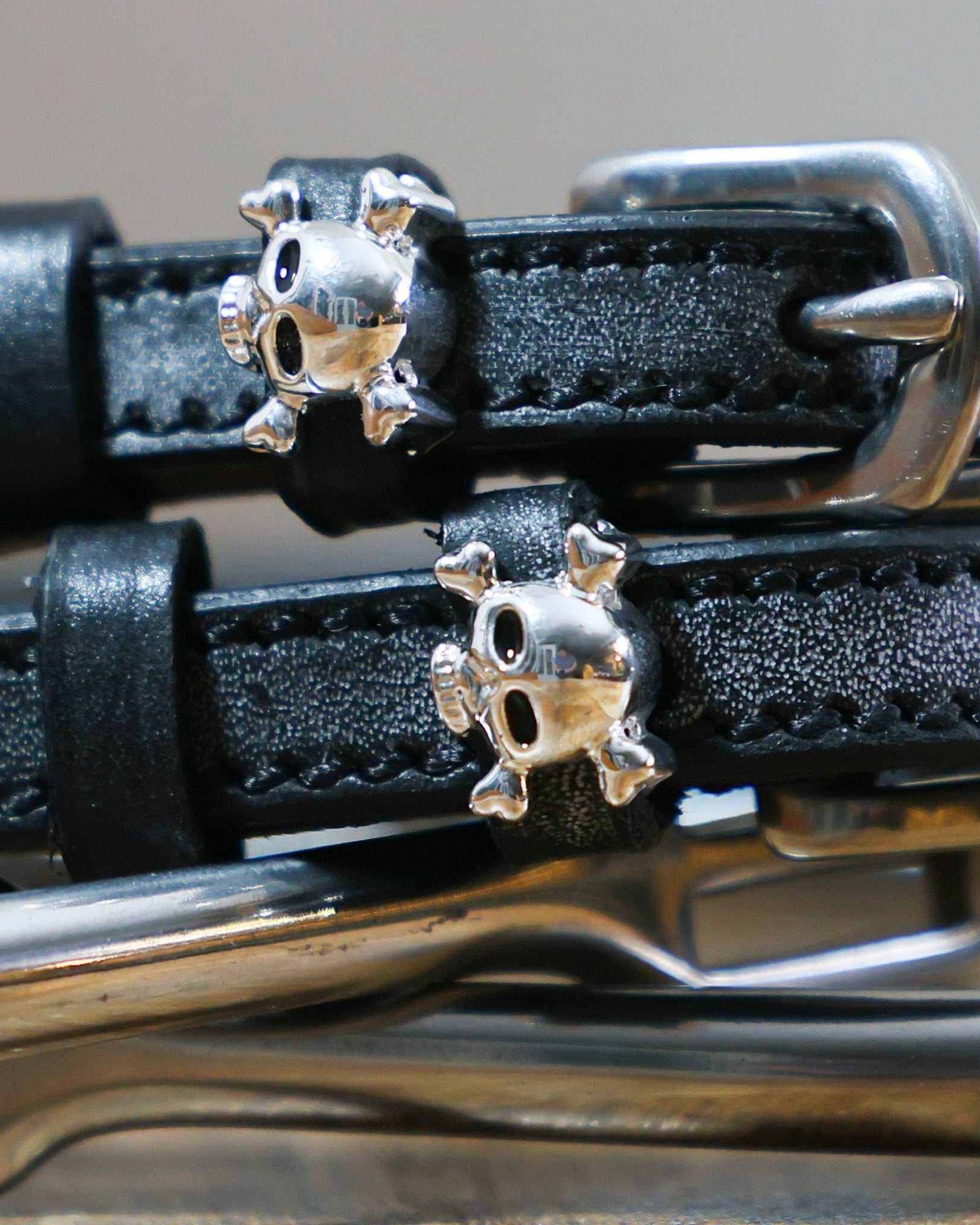Close-up of silver skull and crossbones charms on black leather spur strap keepers
