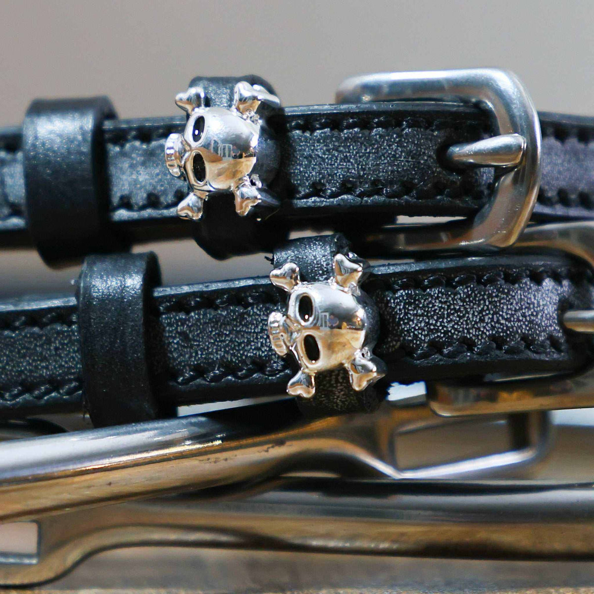 Close-up of silver skull and crossbones charms on black leather spur strap keepers