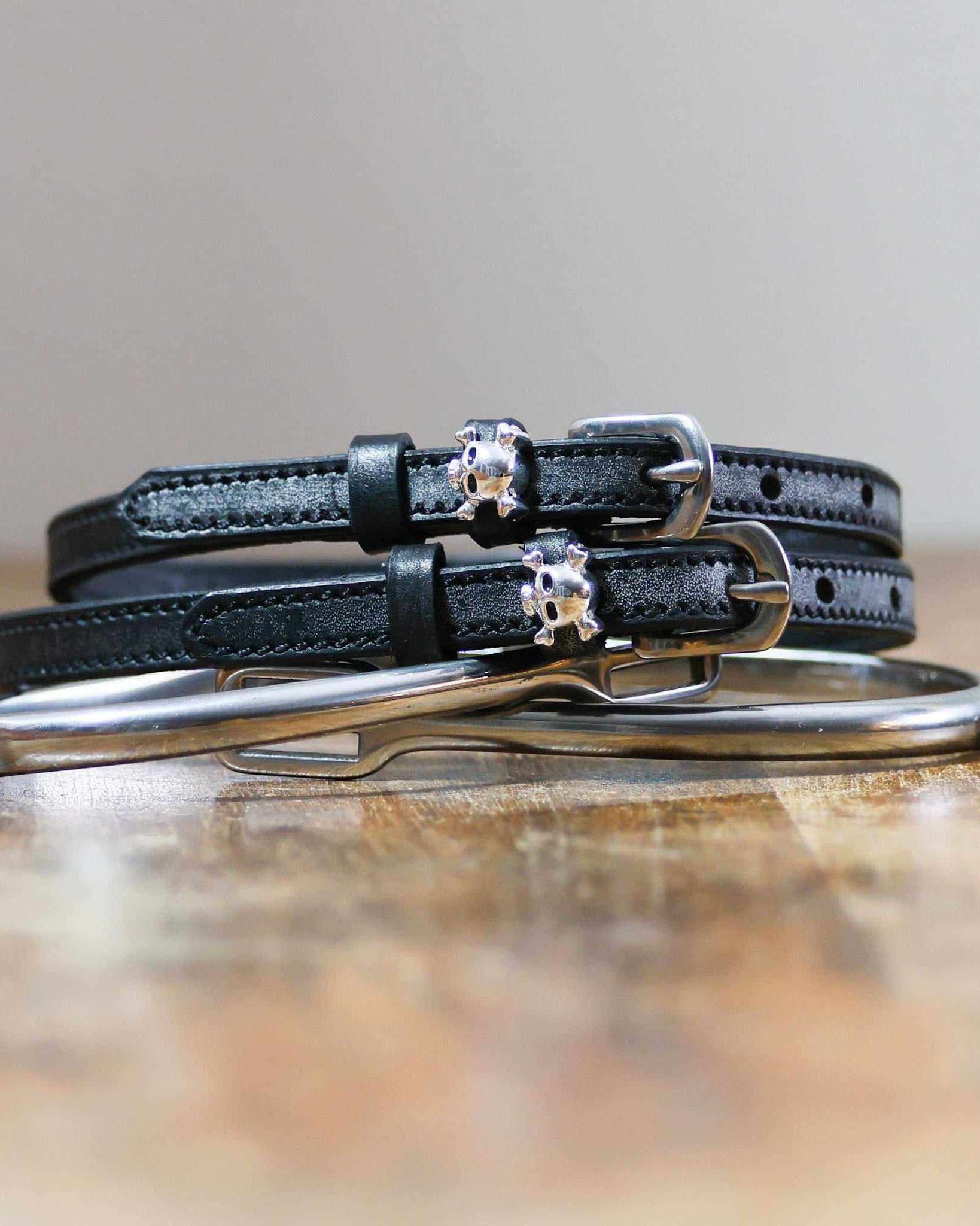 Black leather skull and crossbones spur straps coiled beside a silver spur on wood
