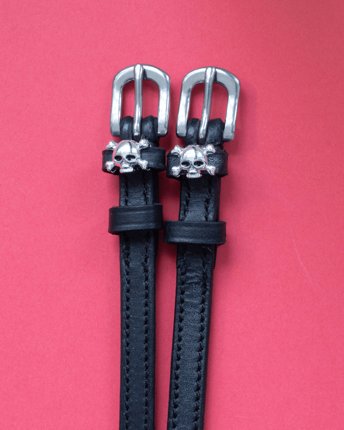 Black leather skull and crossbones spur straps with silver buckles on coral red
