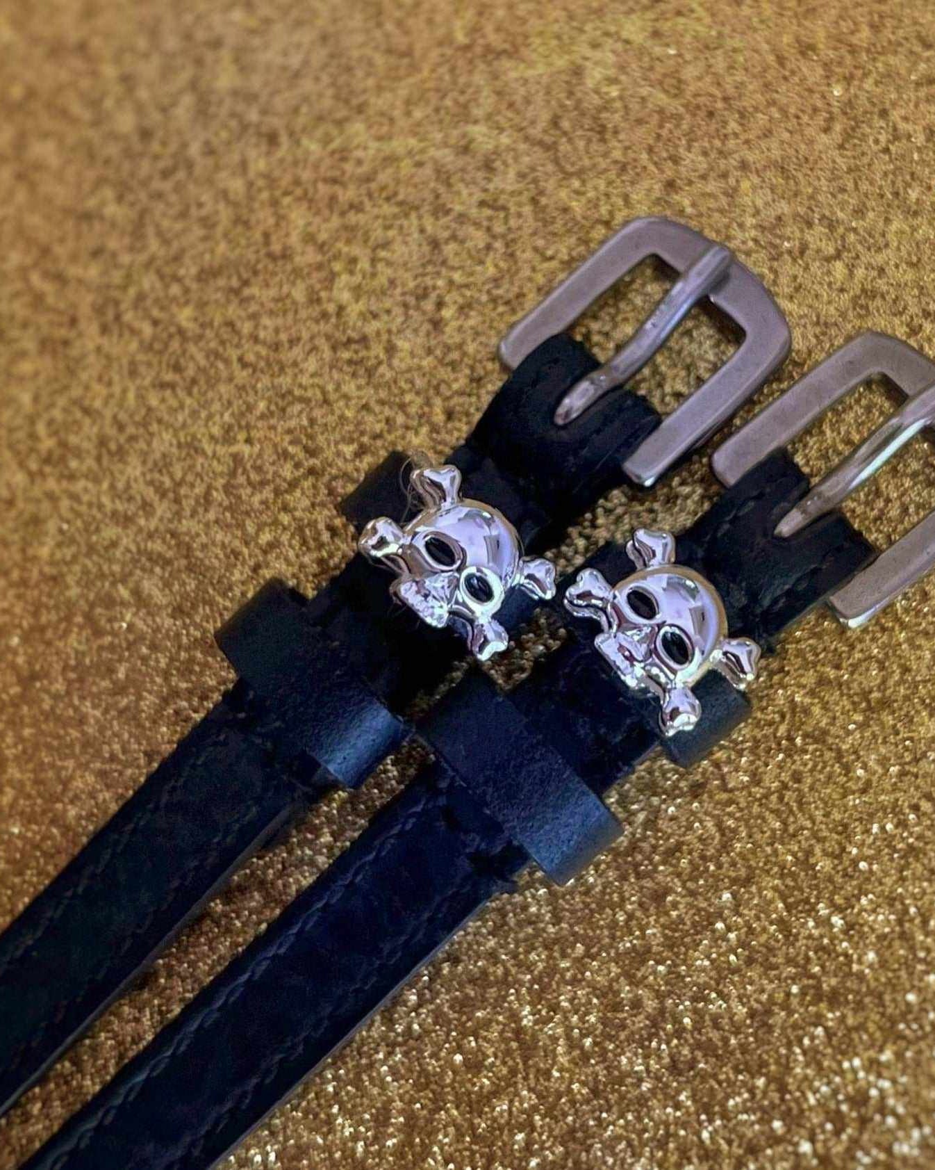 Black leather skull and crossbones ManeJane spur straps on a gold glitter background