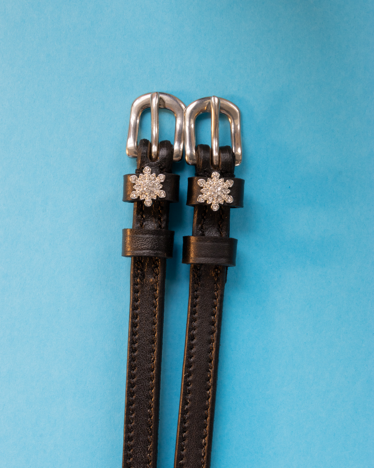 Black snowflake spur straps with rhinestone snowflake charms on a light blue background