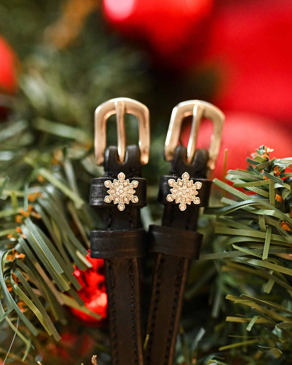 Snowflake spur straps with rose-gold buckles nestled in a pine Christmas wreath, ManeJane