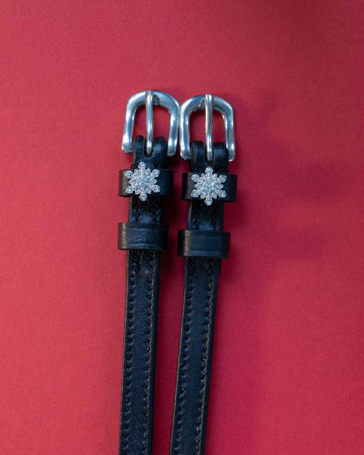 ManeJane snowflake spur straps with rhinestone snowflake charms on a deep red background