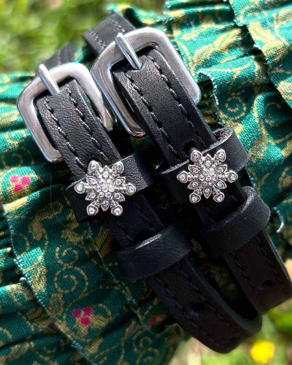 Snowflake spur straps with crystal charms draped over green floral fabric, ManeJane