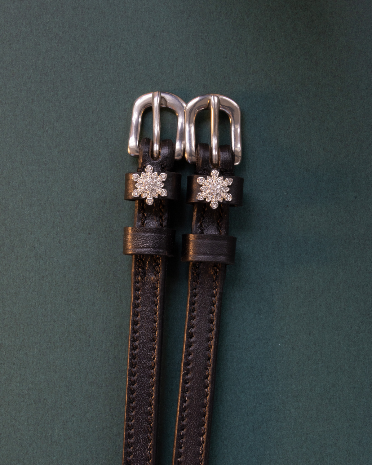 ManeJane snowflake spur straps with crystal snowflake charms on a dark green background