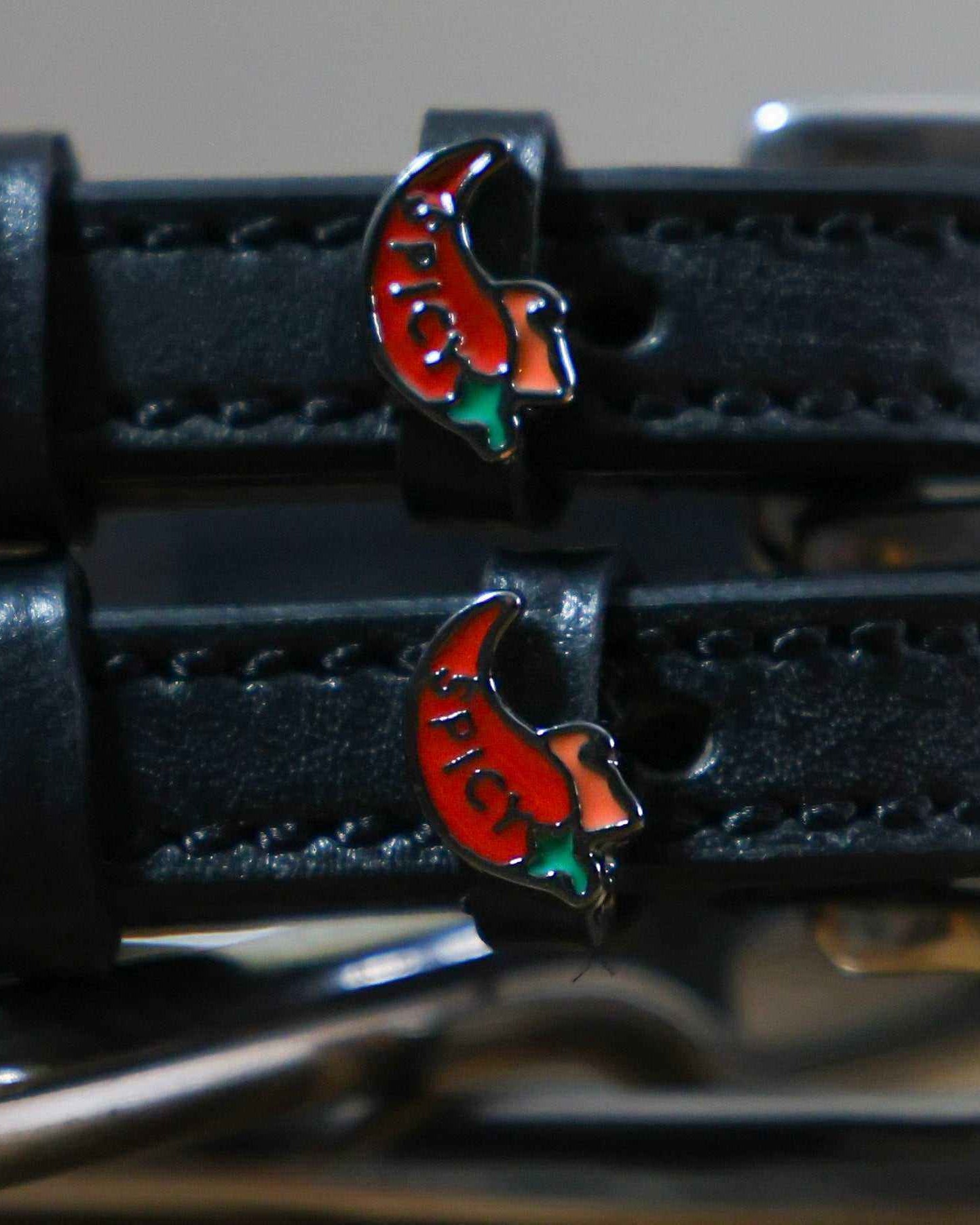 Close-up of red chili pepper charms on black leather ManeJane spur straps, silver spur behind