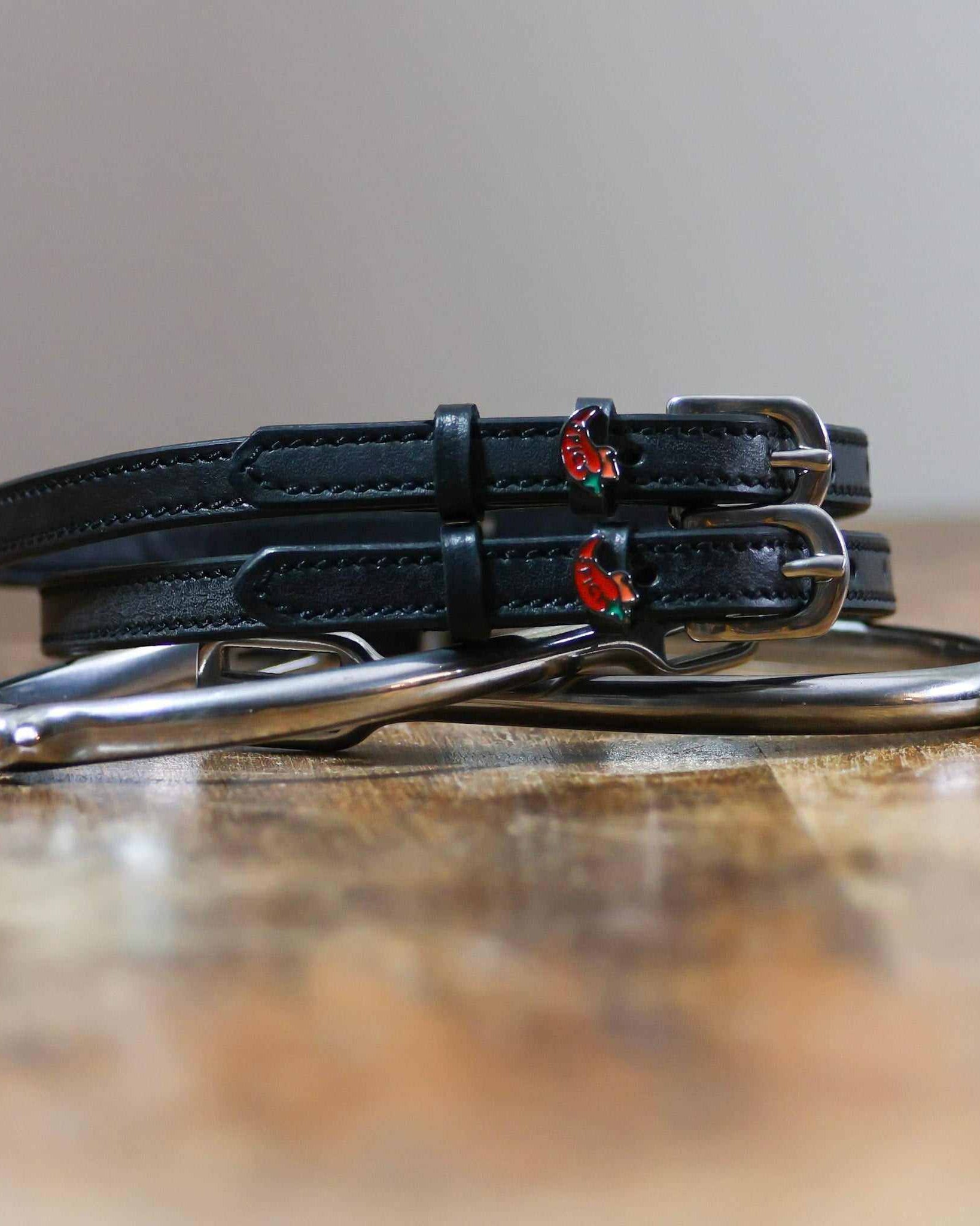 Coiled black leather spicy pepper spur straps resting on a silver spur, red chili charms