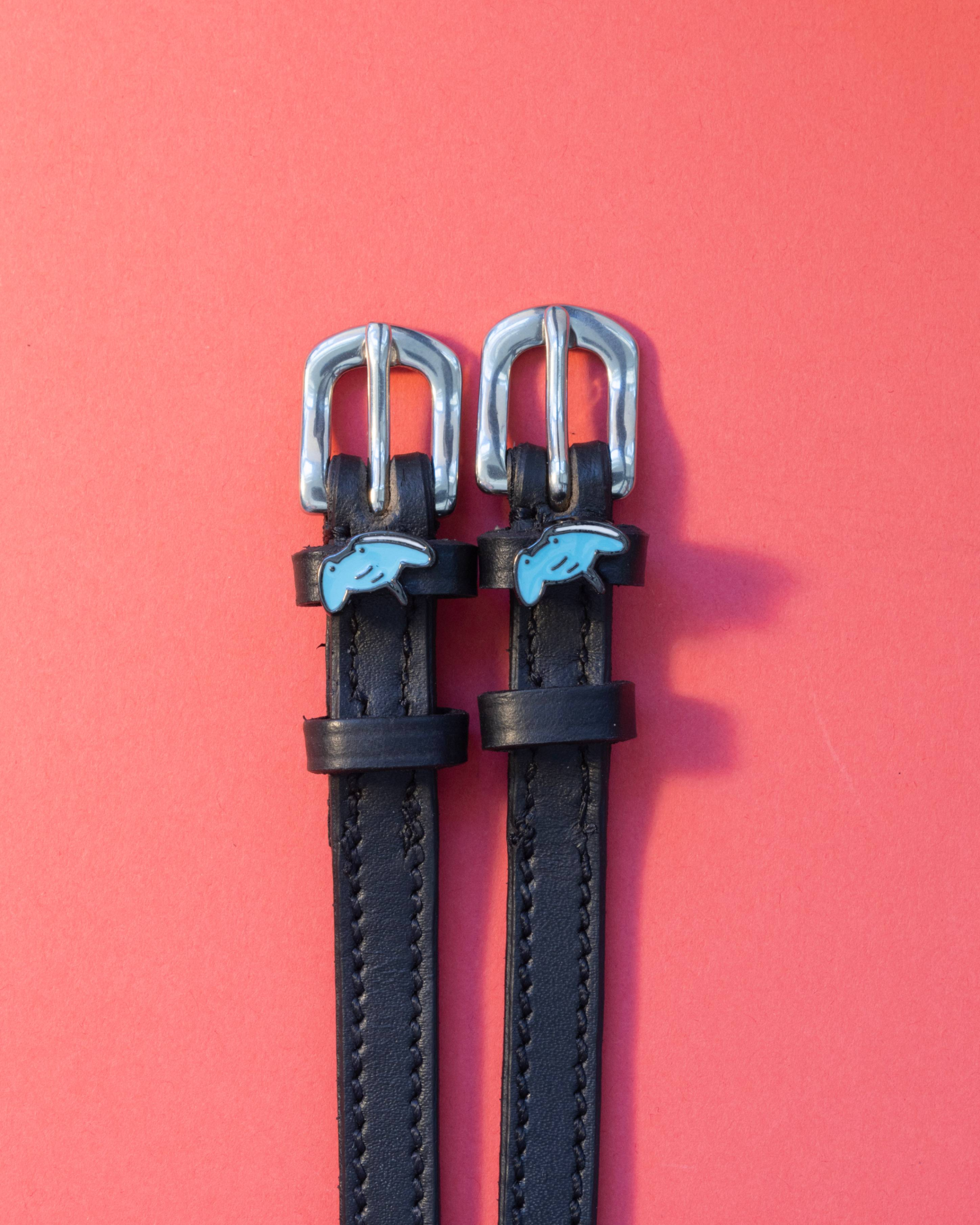 Black leather stingray spur straps with blue ray charms on a coral background, ManeJane