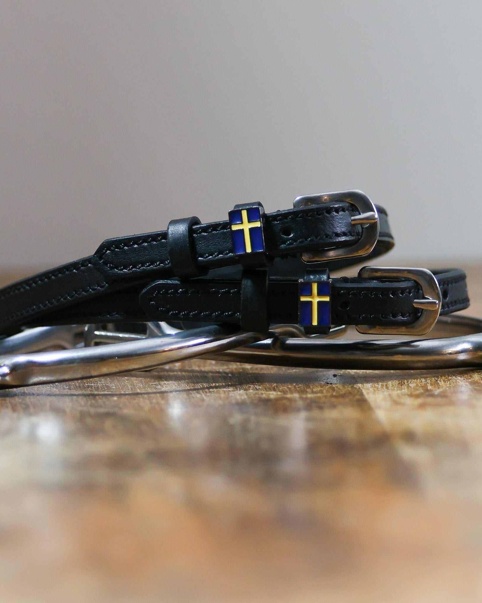 Black leather Swedish flag spur straps coiled beside a spur on wood