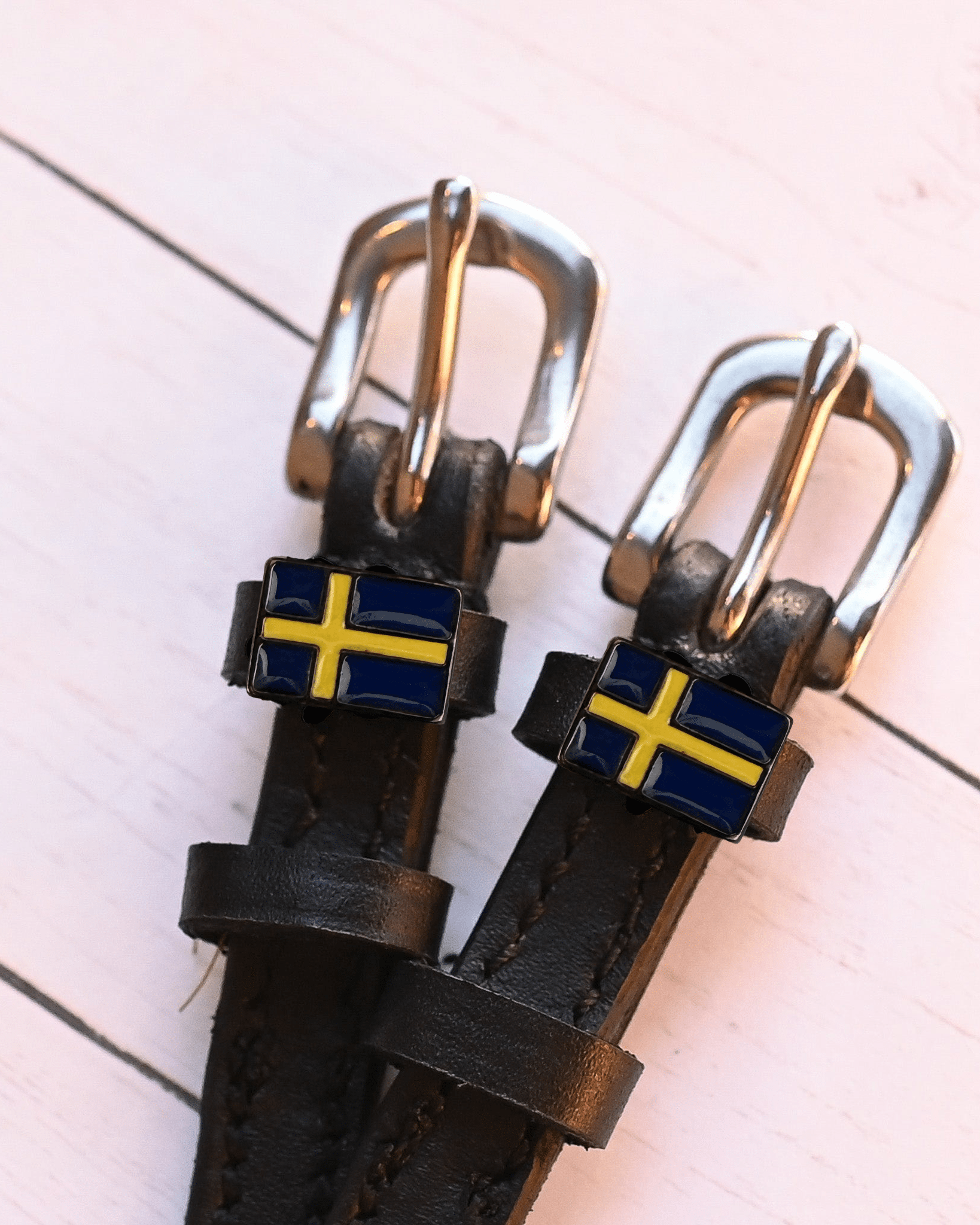 Two Swedish flag charms on dark leather spur straps over pink planks